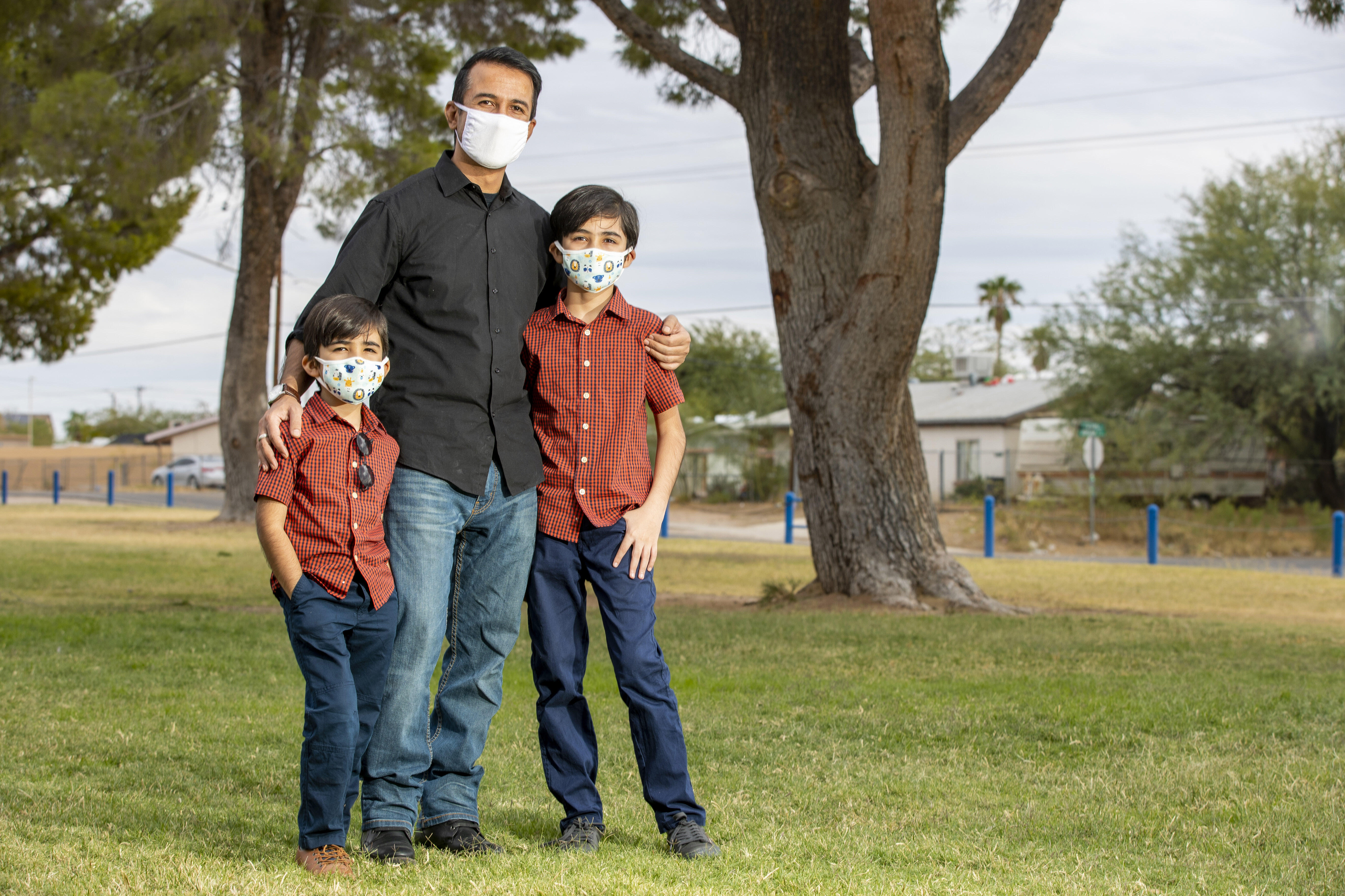 A man stands with his arms around his two young sons in Pima County, Arizona. They are wearing facemasks to protect them from COVID-19.