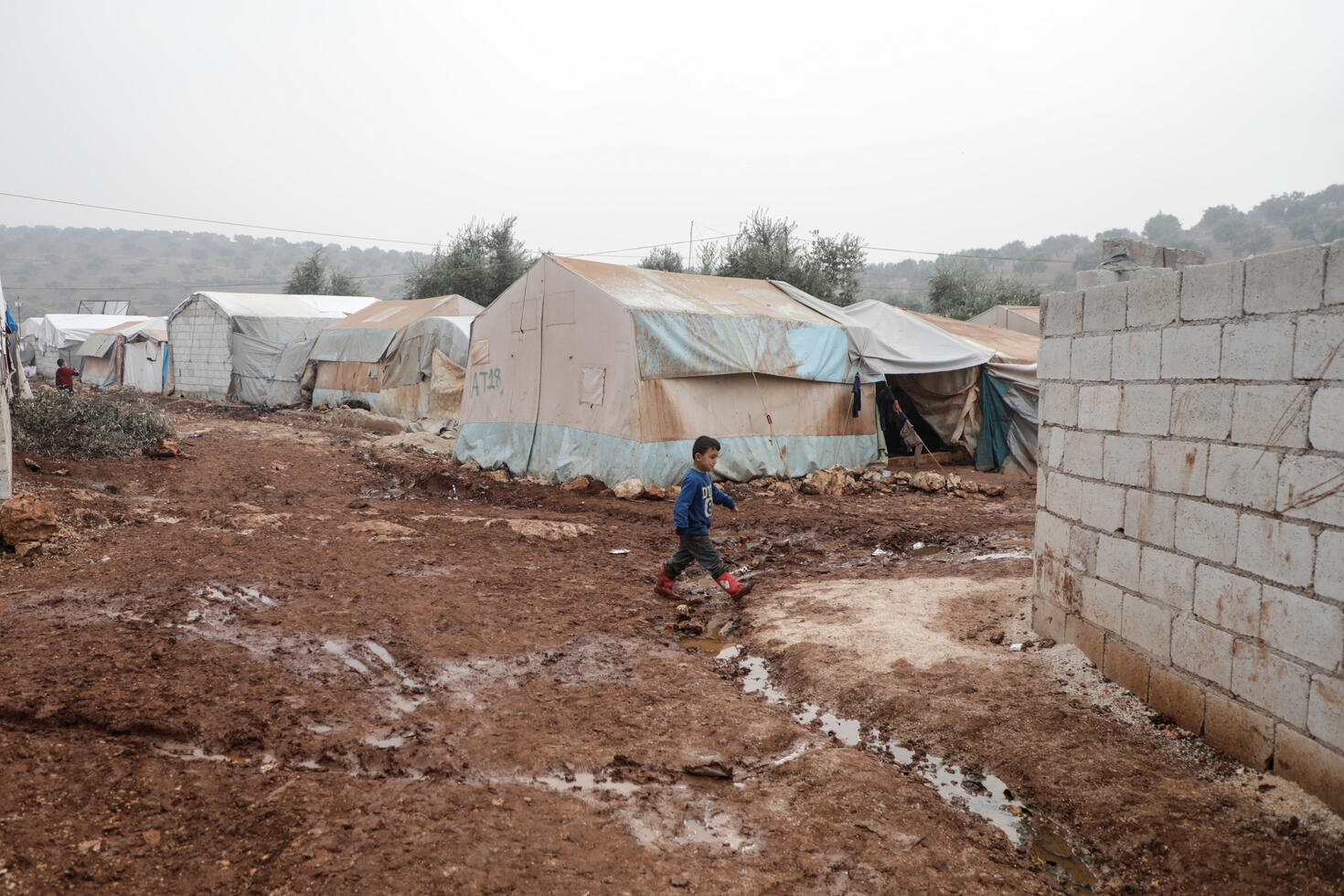 A Syrian boy walks through the mud past tents for displaced families in Idlib, where the IRC provides aid.