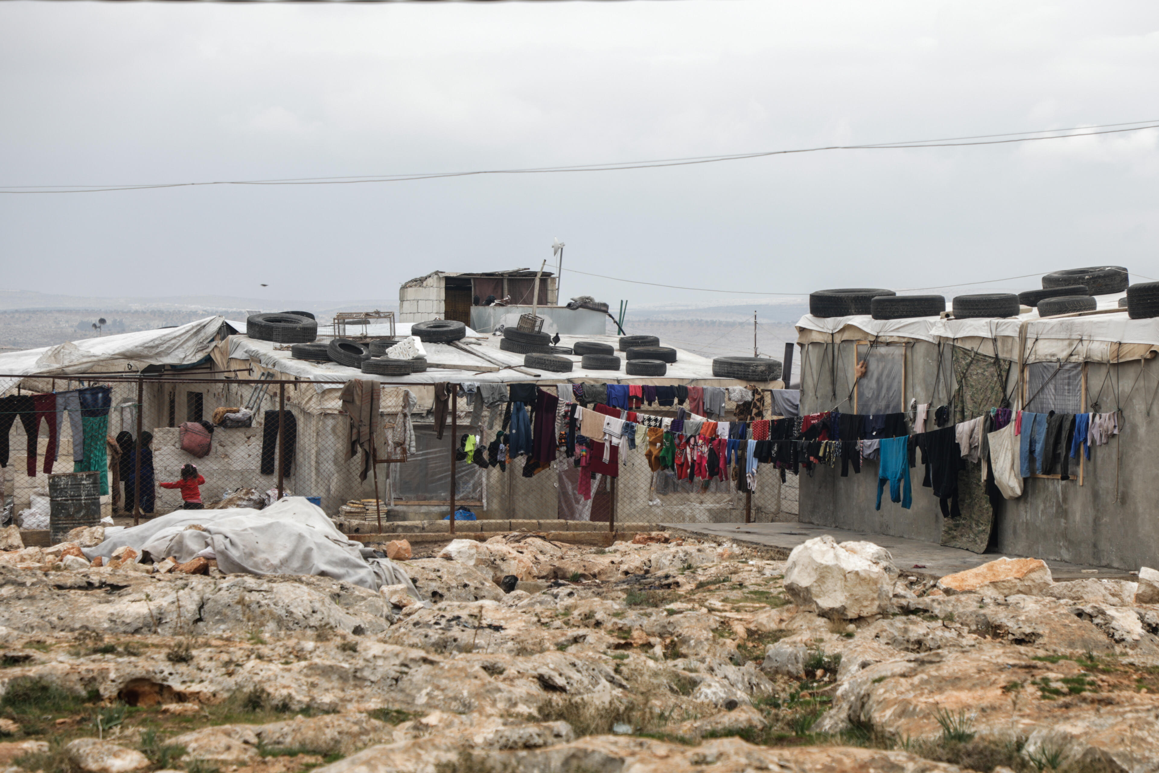 Women and children stand near clothes hanging to dry in a settlement where the IRC is assisting displaced people on the outskirts of the town of Deir Hassan.