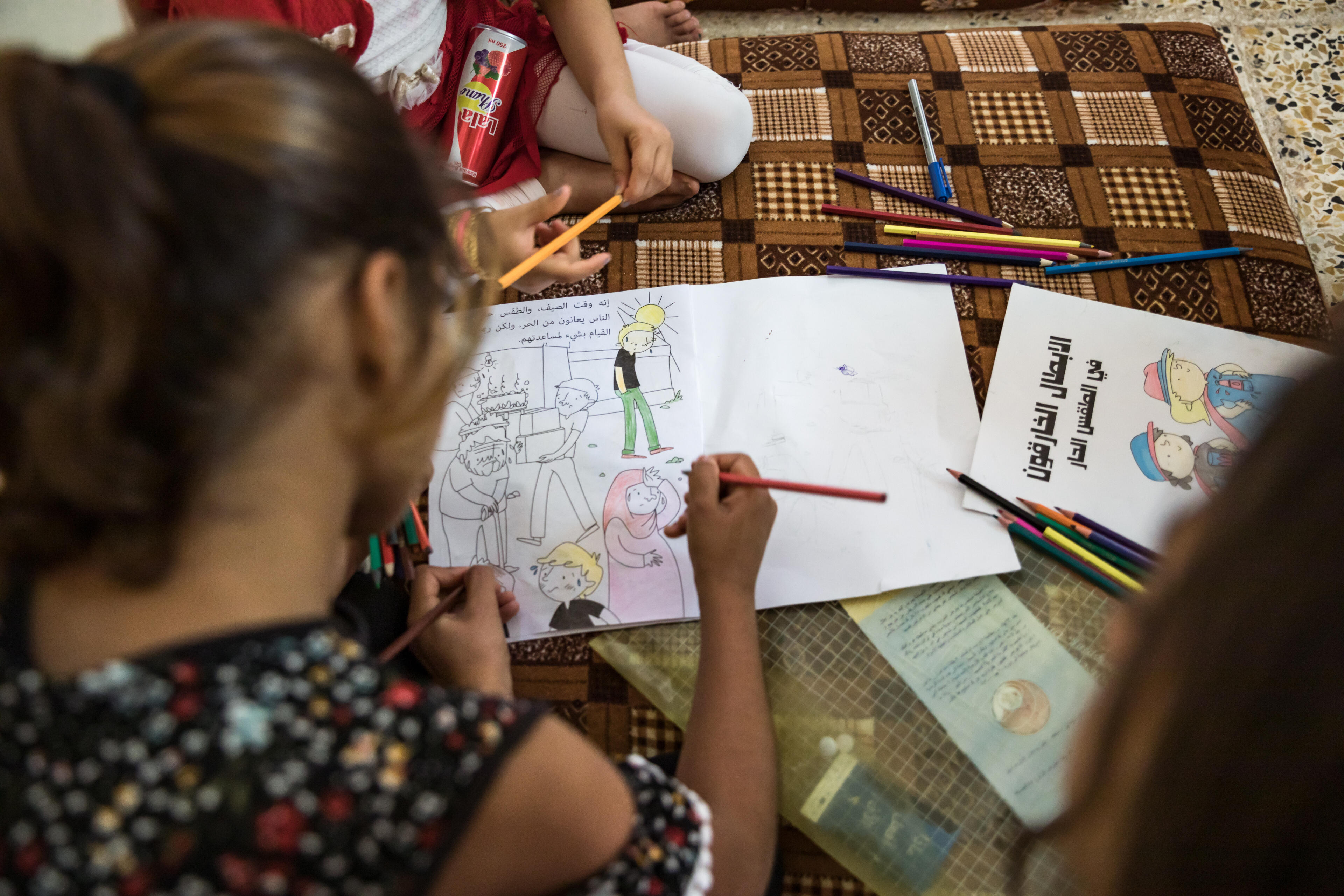 Children in Sinjar, Iraq sit on the floor of their home, coloring