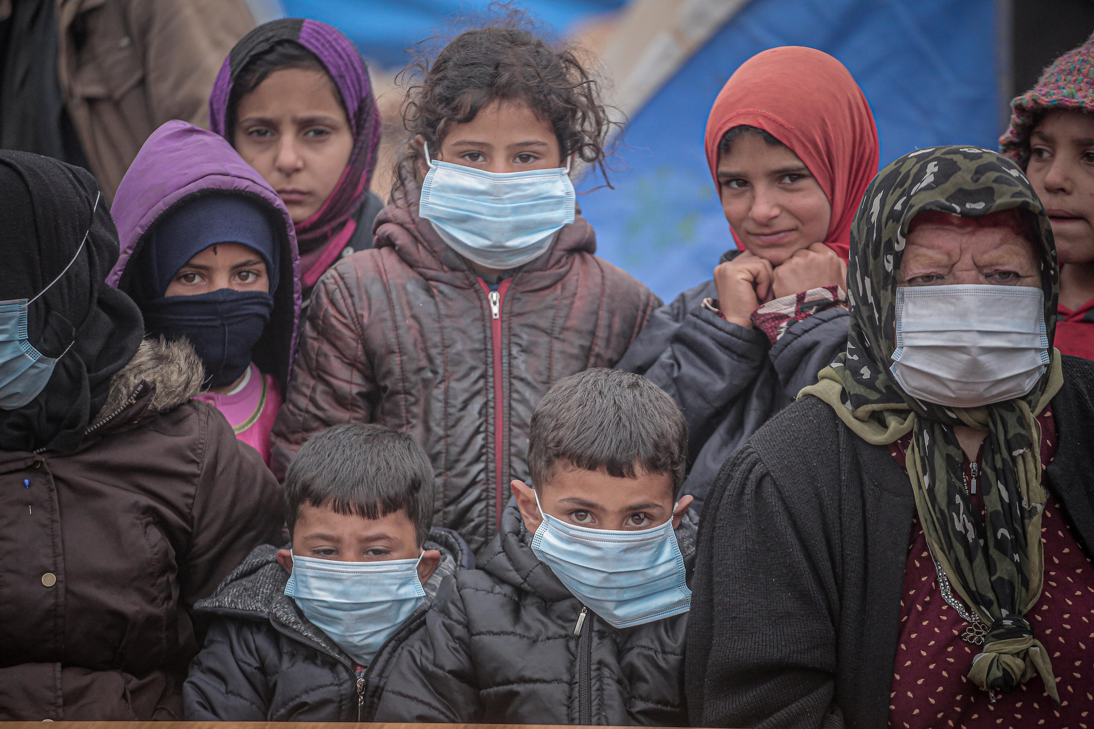 A group of displaced children with an older woman wearing face masks during the COVID-19 pandemic