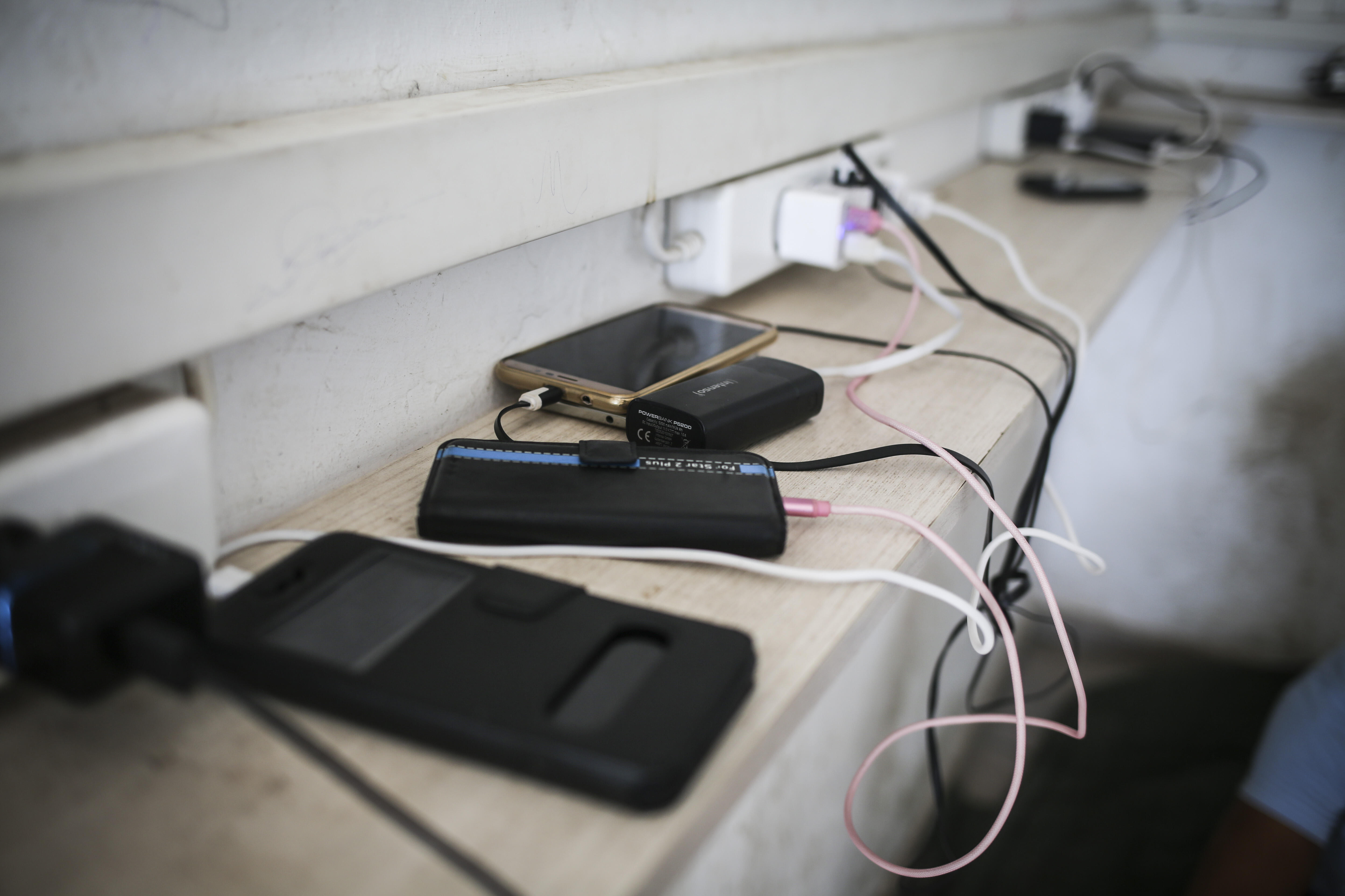 Refugees' ell phones and battery packs charge on a ledge in a refugee camp in Greece