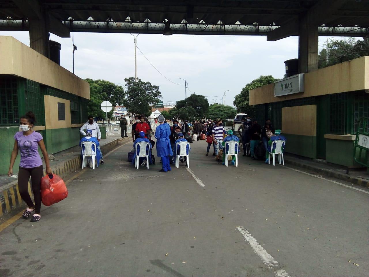 Heath care workers in scrubs sit on chairs or stand offering services to Venezuelans crossing the Simon Bolivar bridge.