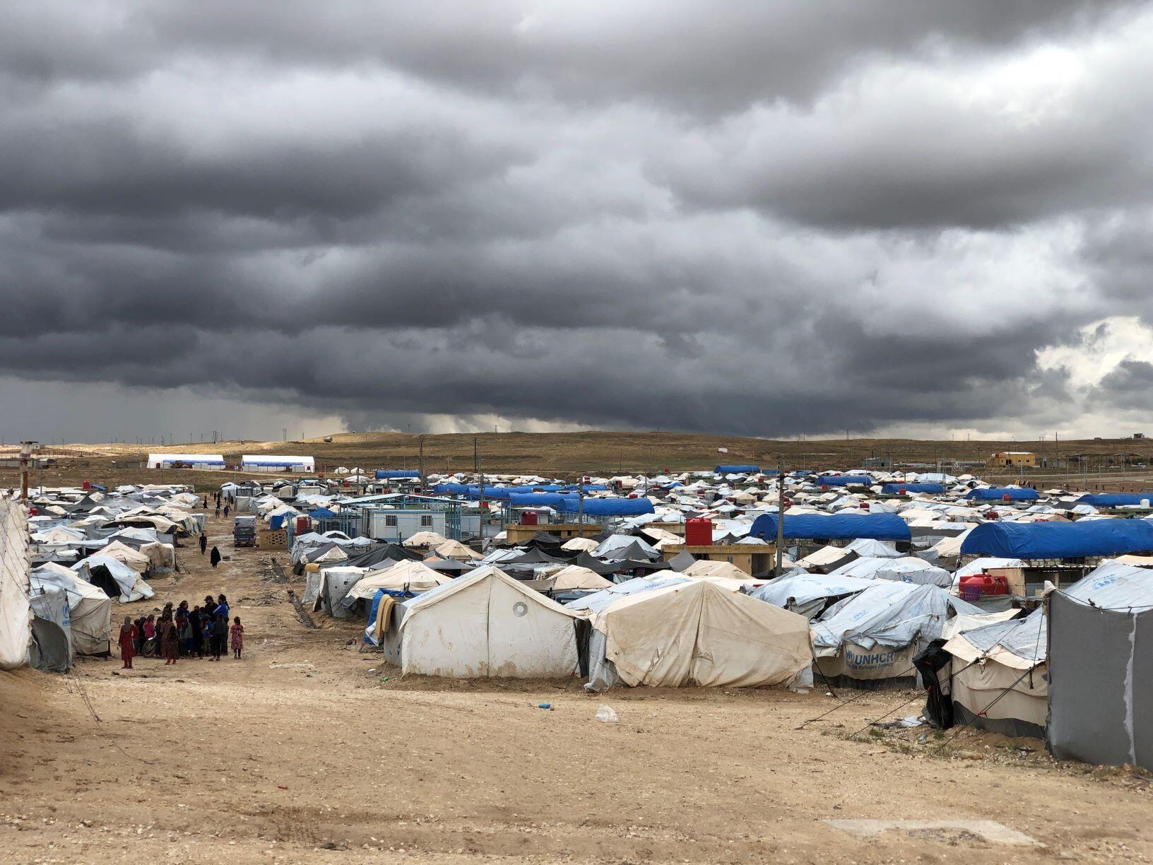Al Hol camp in northeast Syria. A group of refugees stand next to a cluster of tents. 