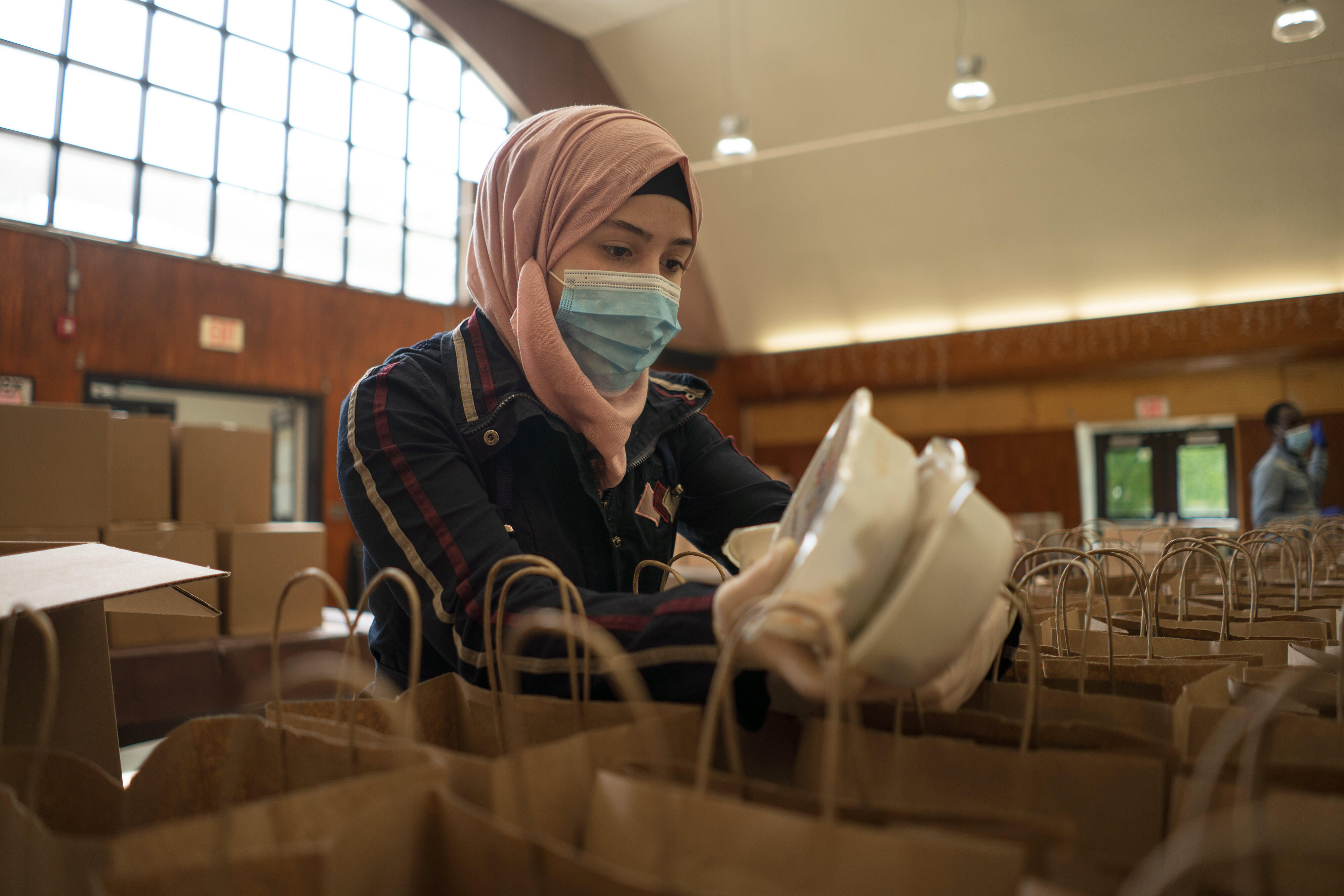 Rania Abou, wearing a mask, puts two containers of food inside paper bags to be given away as part of her work with the IRC and World Central Kitchen.