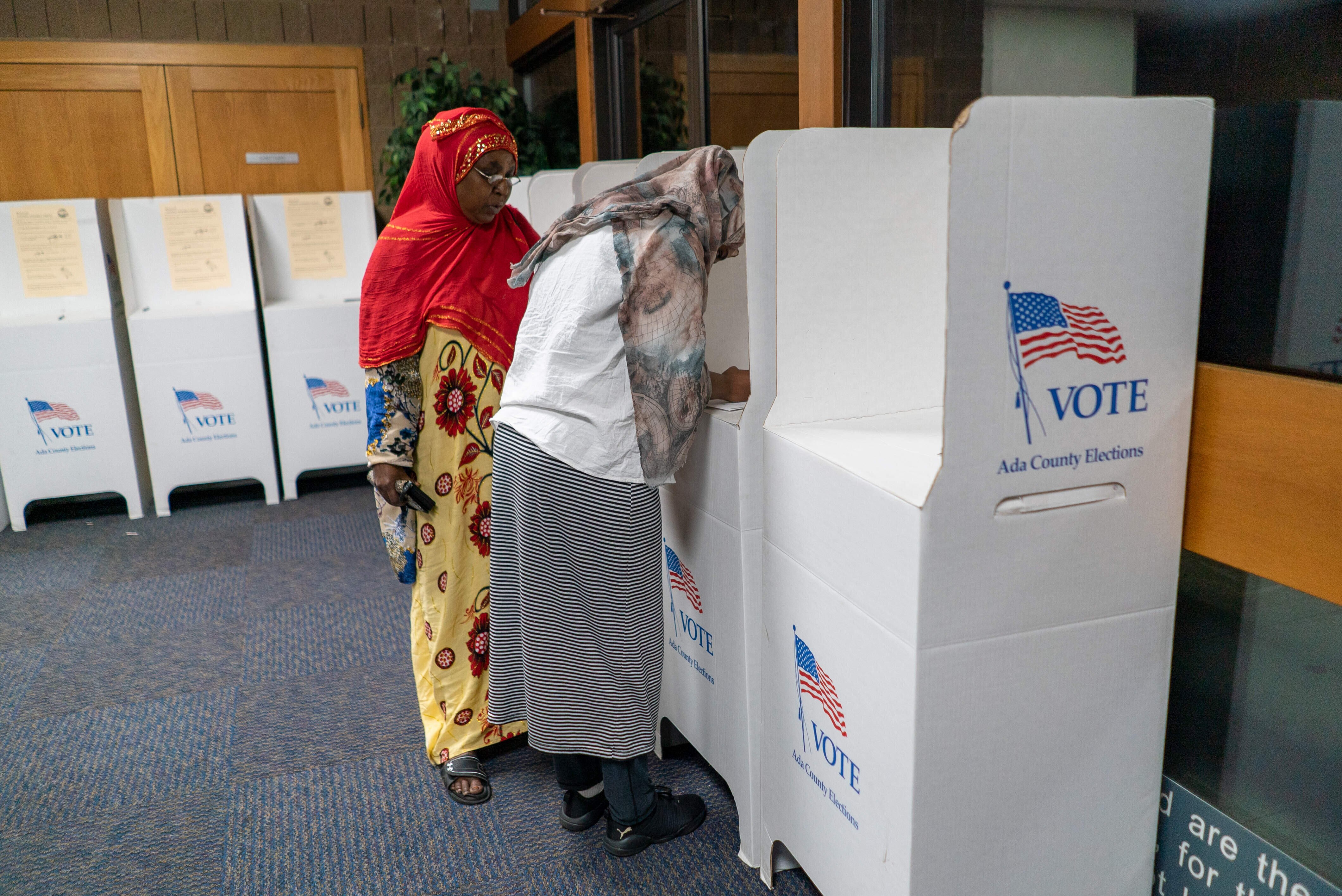 Two woman vote in an election in Boise, Idaho. One is filling out her ballot in a privacy booth while the other stands next to her.