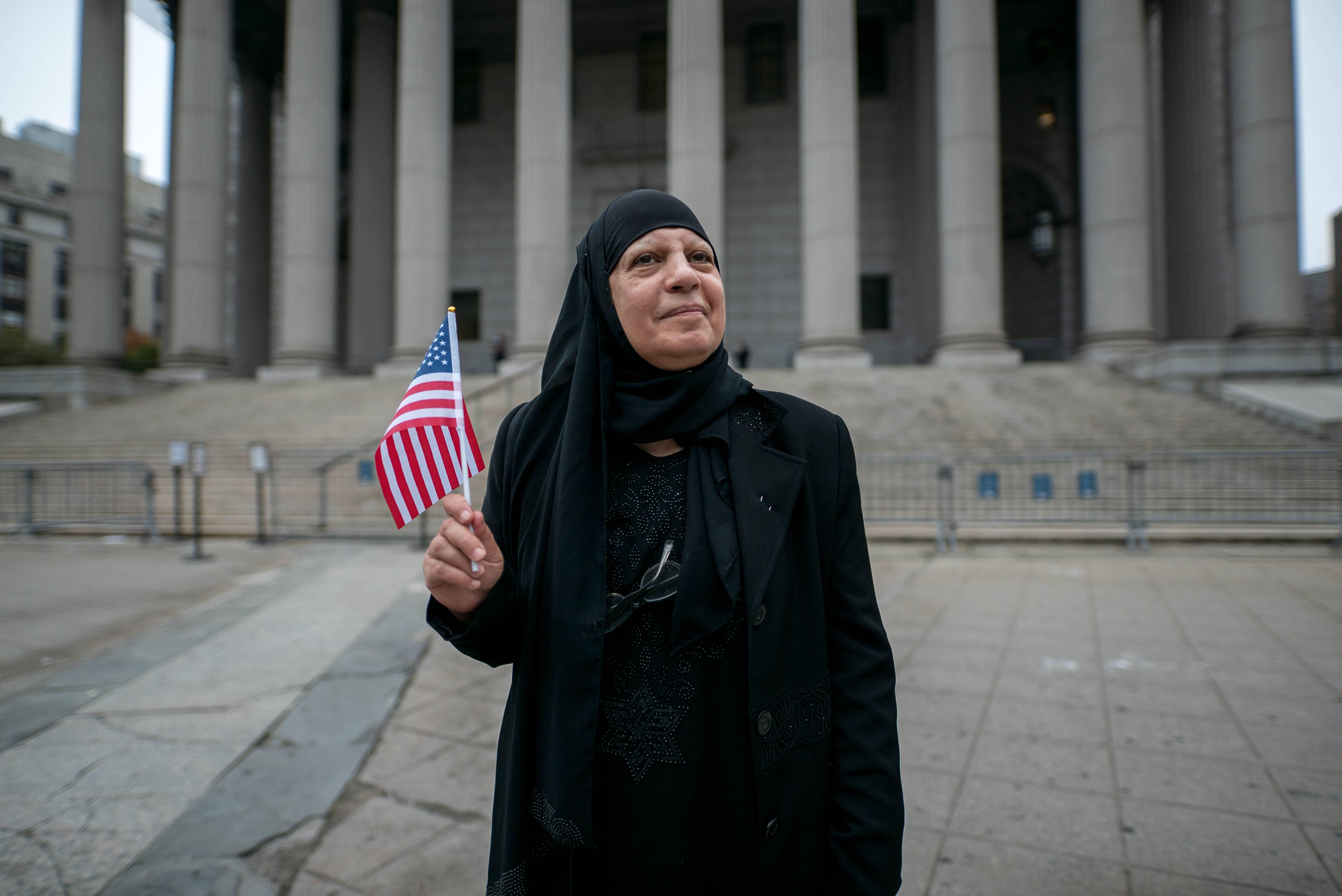 Maha al-Obaidi stands in front of a government building holding an American flag. 
