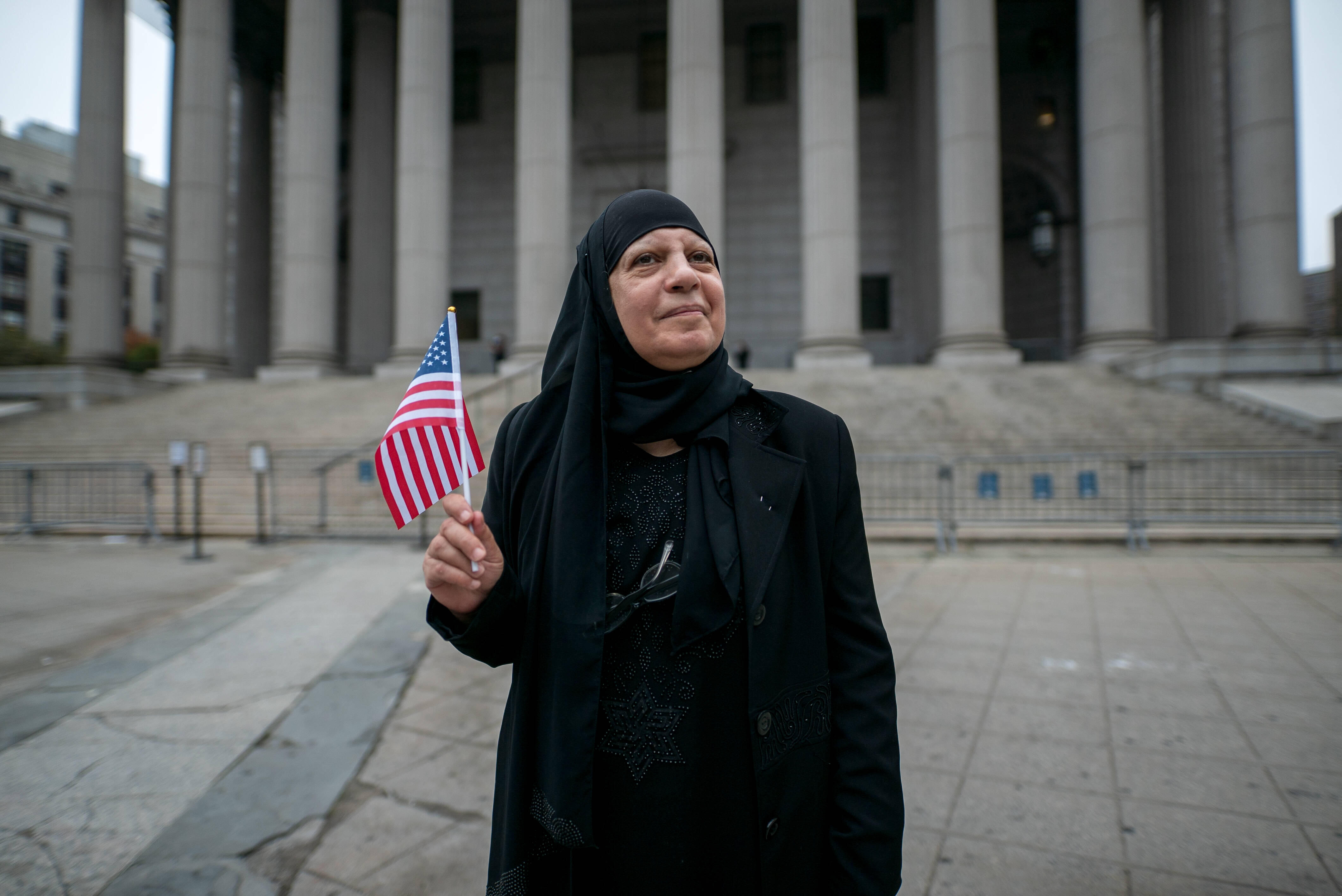 Maha al-Obaidi stands in front of a government building holding an American flag.