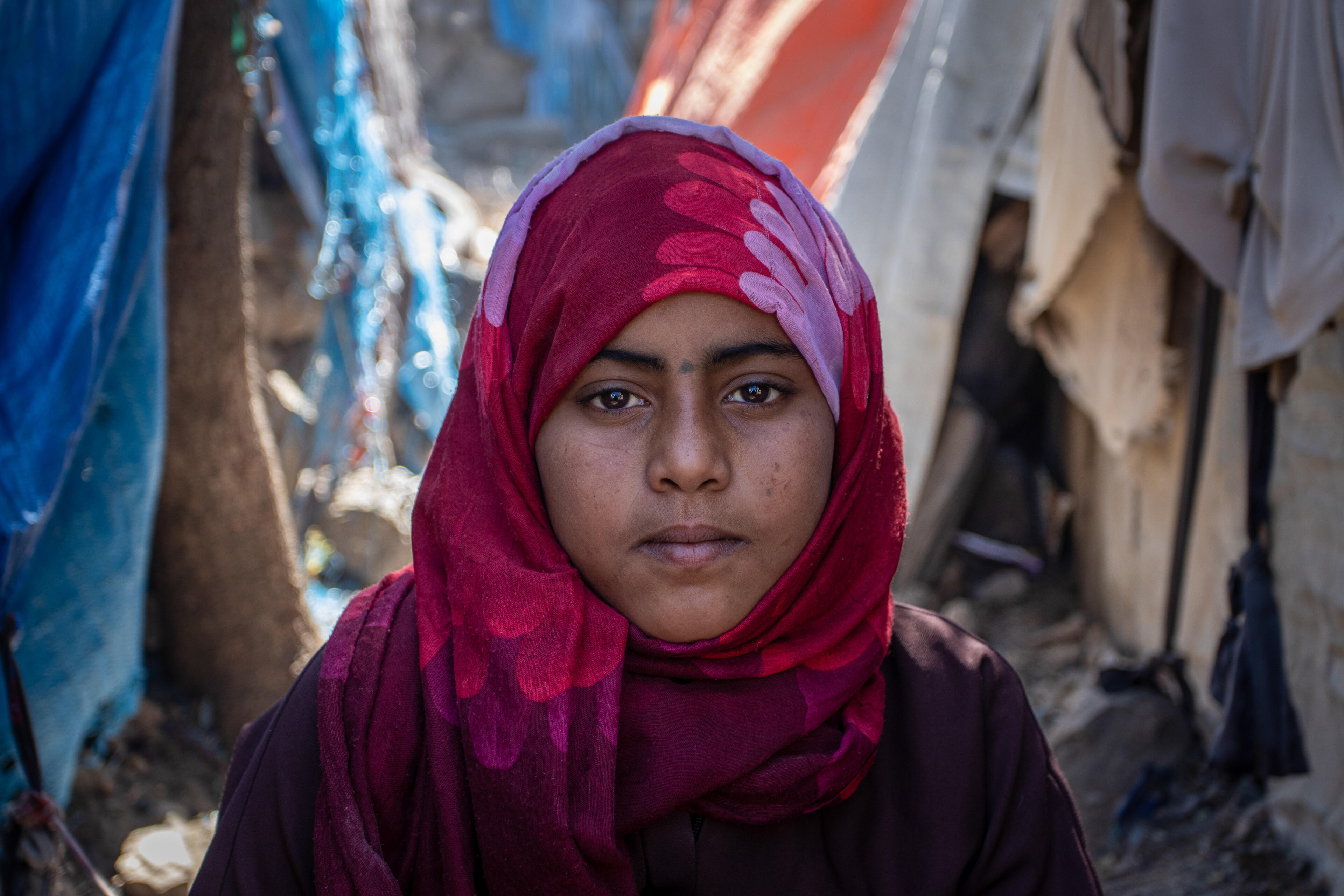 A displaced 11-year-old Yemeni girl named Na'aem stands amid makeshift tents looking directly at the camera with a serious expression.