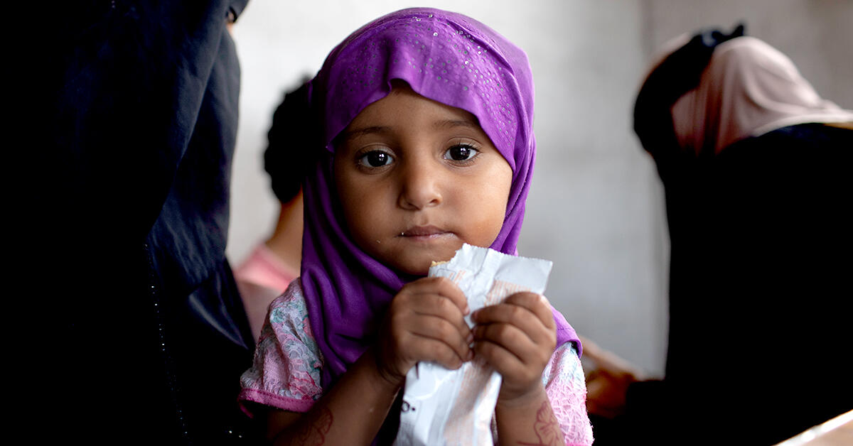 In Yemen, a young girl being treated for acute malnutrition eats Plumpy'nut, a peanut butter based nutritional paste, from a packet.