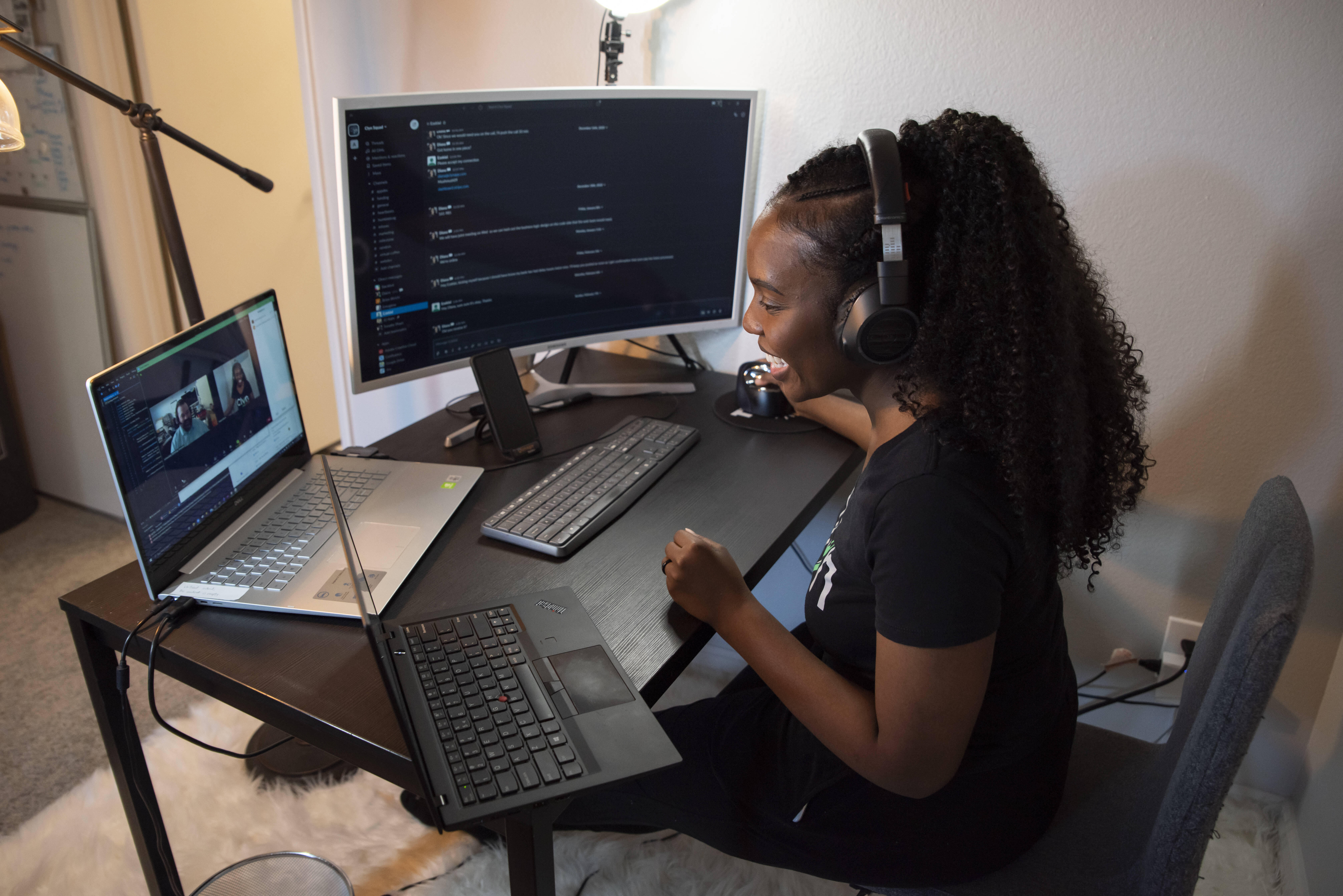 Wearing headphones, Diana Muturia smiles and looks at her computer while working on her app, Clyn. 