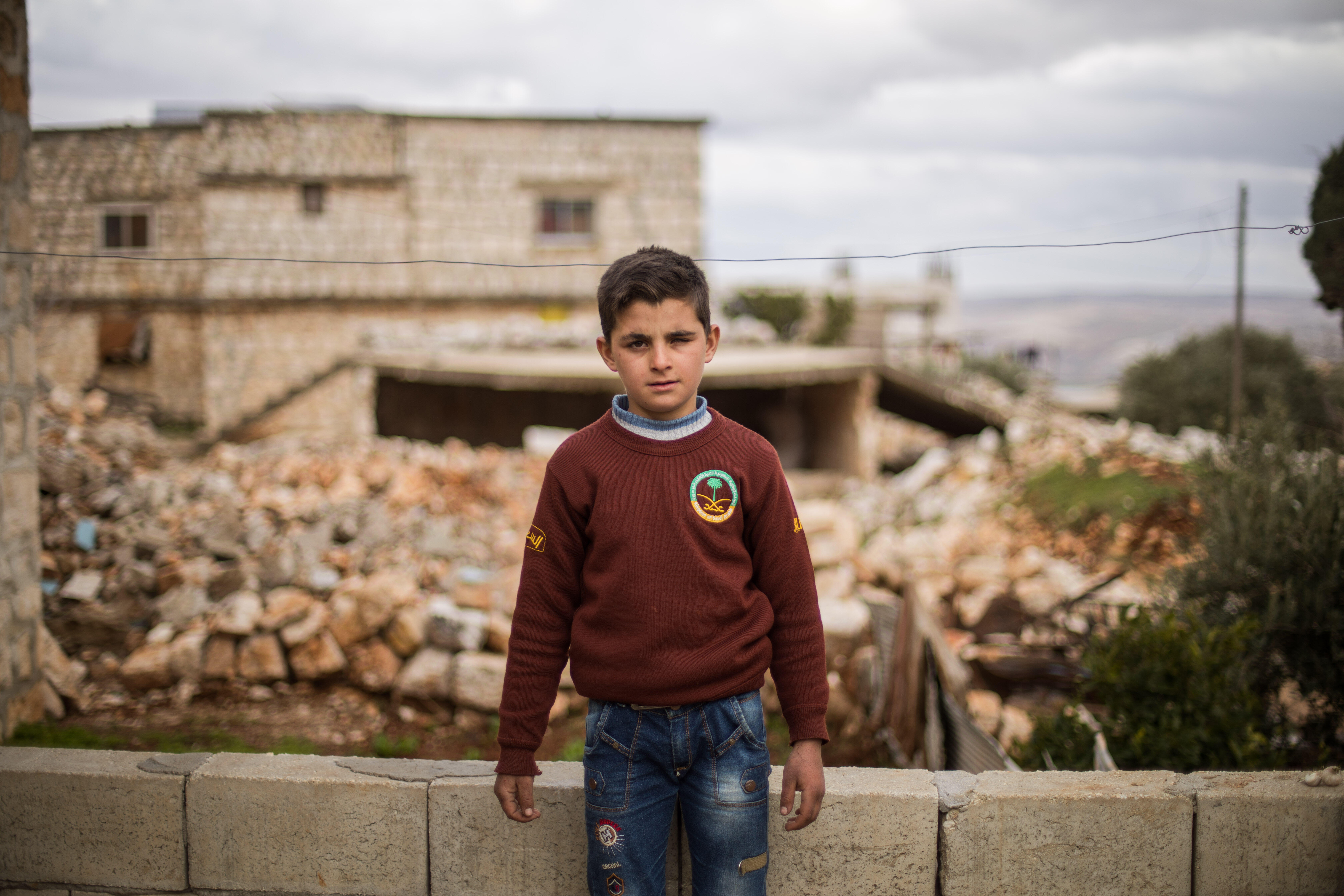 Ten-year-old Ali stands in front of his family's home, which was damaged by an airstrike. 