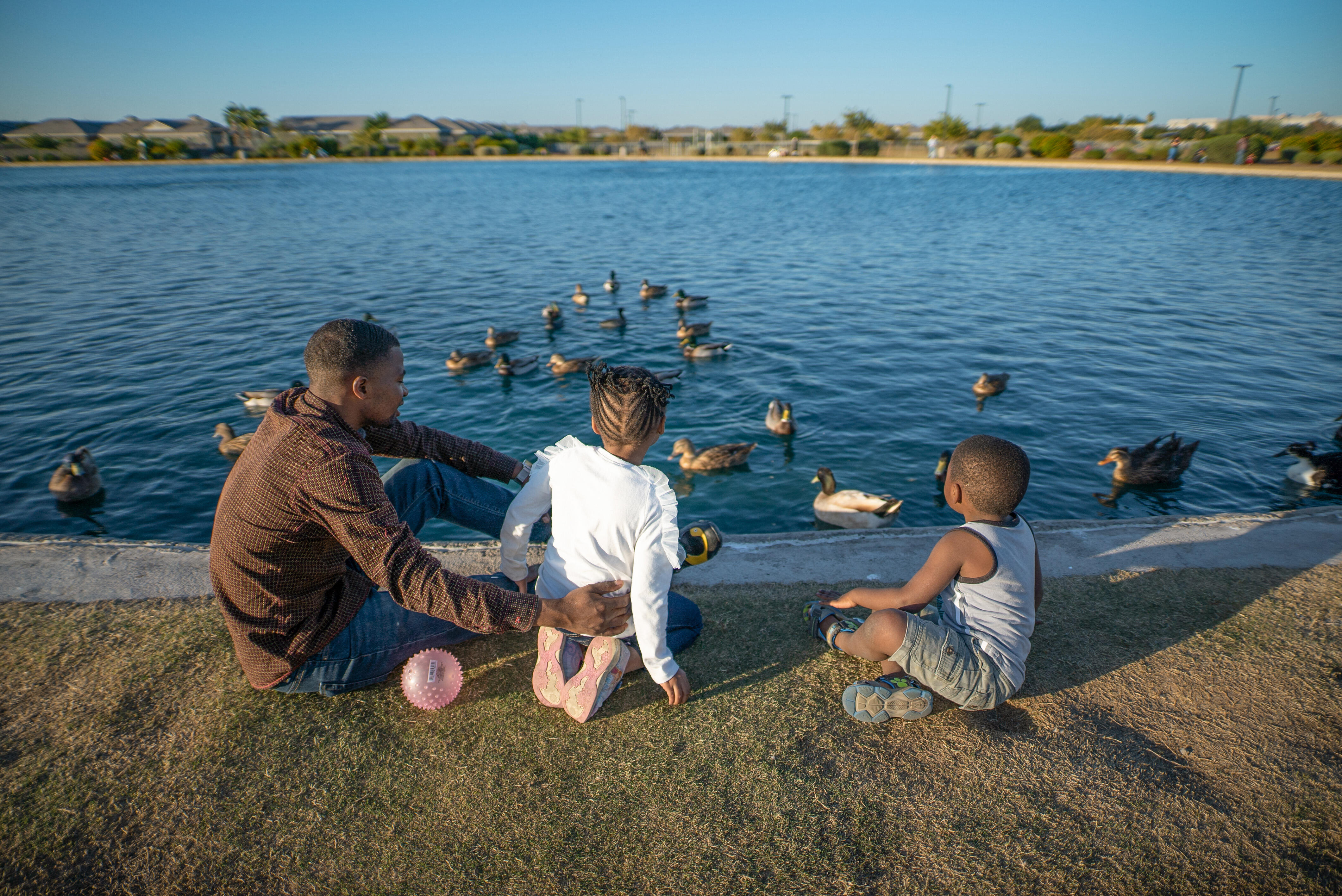 Congolese refugee Robert Sebatware sits with his two young children watching ducks swim in a pond in Phoenix, Arizona