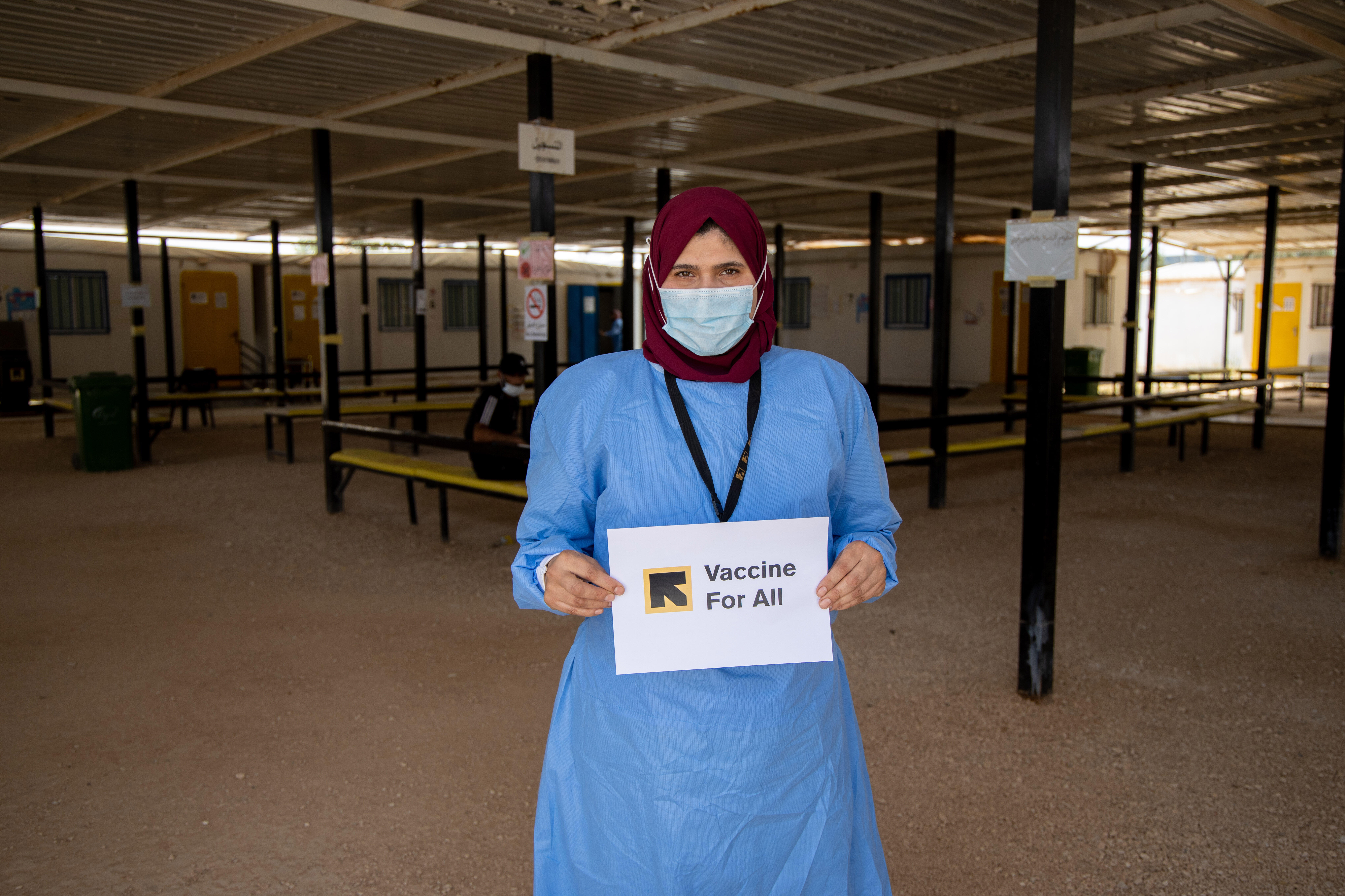 Hend Abu Dabour, an IRC nurse, holds up a sign saying Vaccine For All in the waiting area at the IRC's clinic in Zaatari refugee camp, Jordan