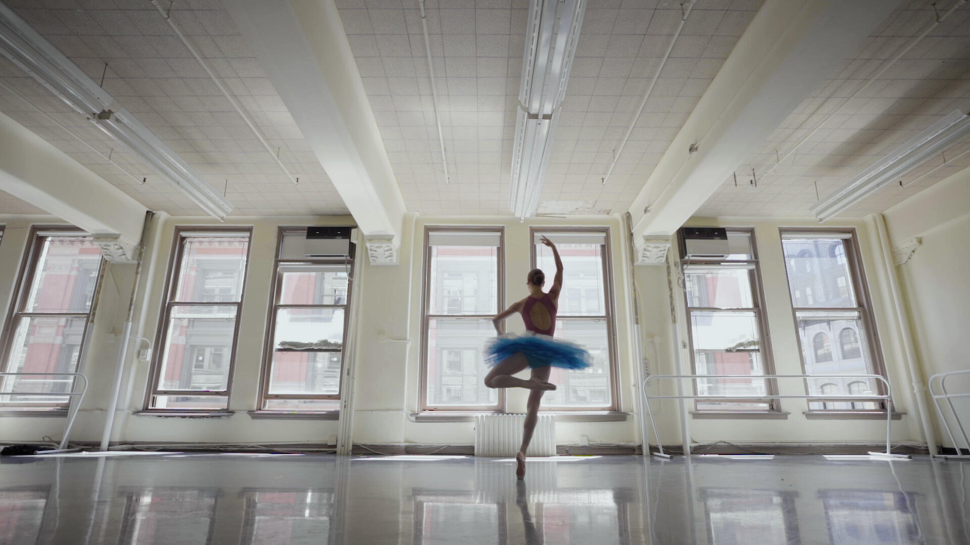 Ballet dancer Christine Shevchenko, wearing a tutu, pirouettes before the windows of a rehearsal studio. 