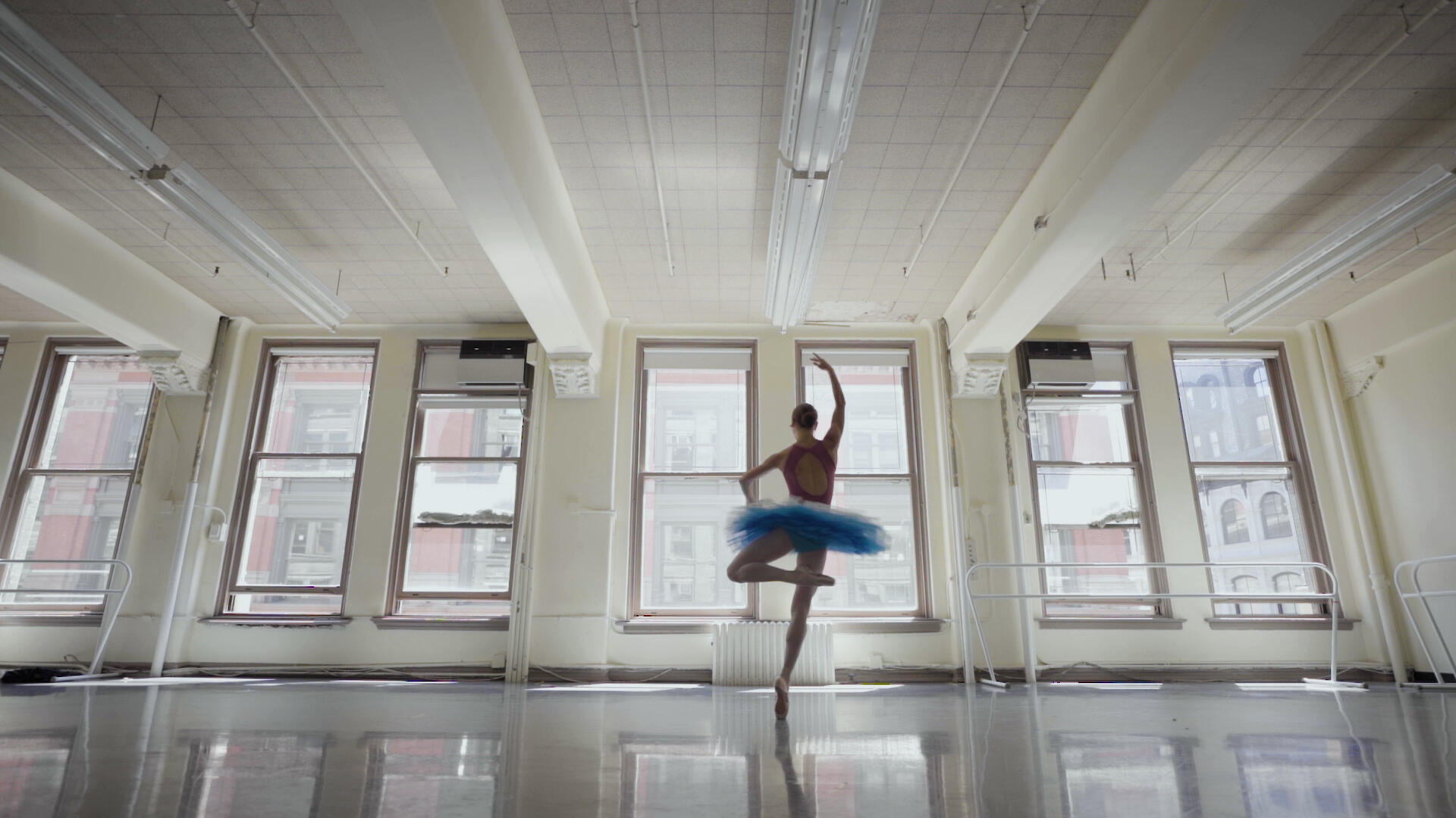 Ballet dancer Christine Shevchenko, wearing a tutu, pirouettes before the windows of a rehearsal studio.