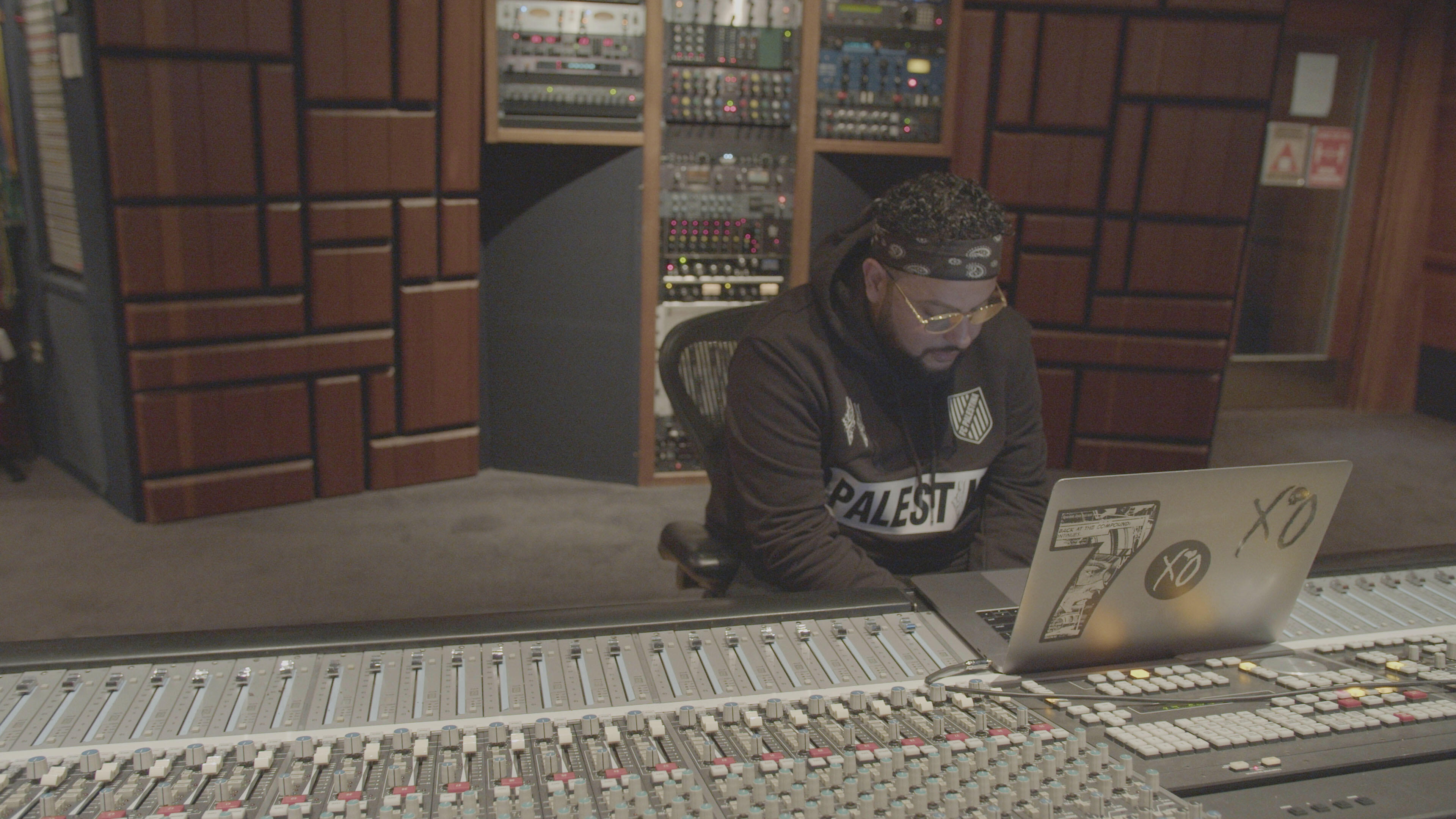 Belly, wearing a headband and a "Palestine" sweatshirt, sits at his laptop, which is perched on a mixing board in a recording studio.