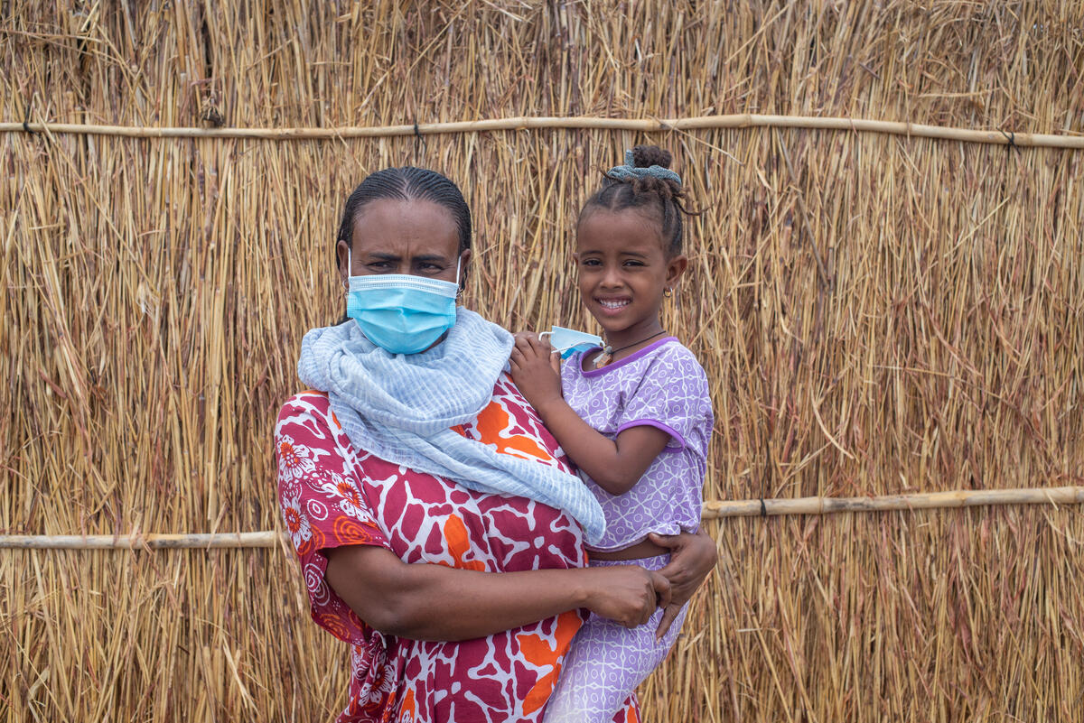 30-year old Azmera from Tigray holds her young daughter outside her thatched shelter in Sudan.