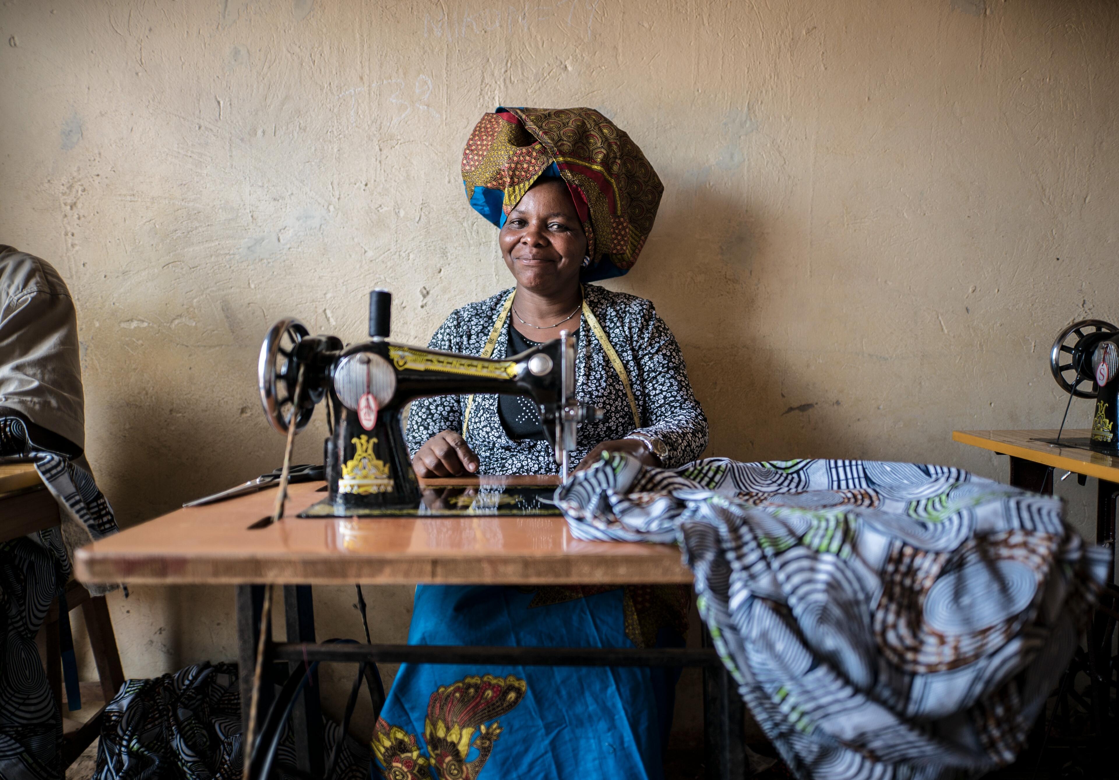 Domitila Kaliya, a Congolese refugee, sits smiling at her sewing machine with fabric in front of her