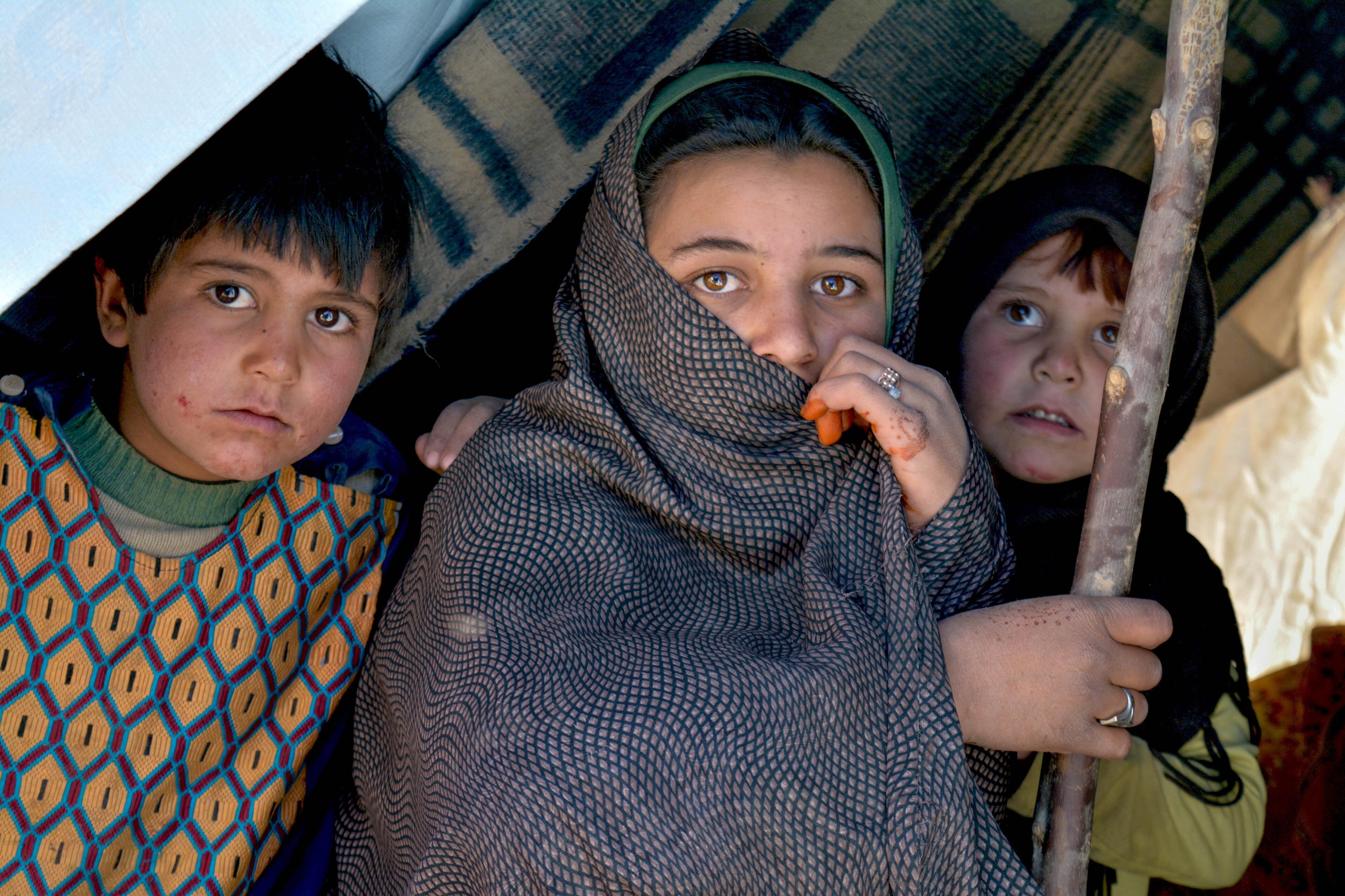 Three Afghan children sit inside a makeshift tent