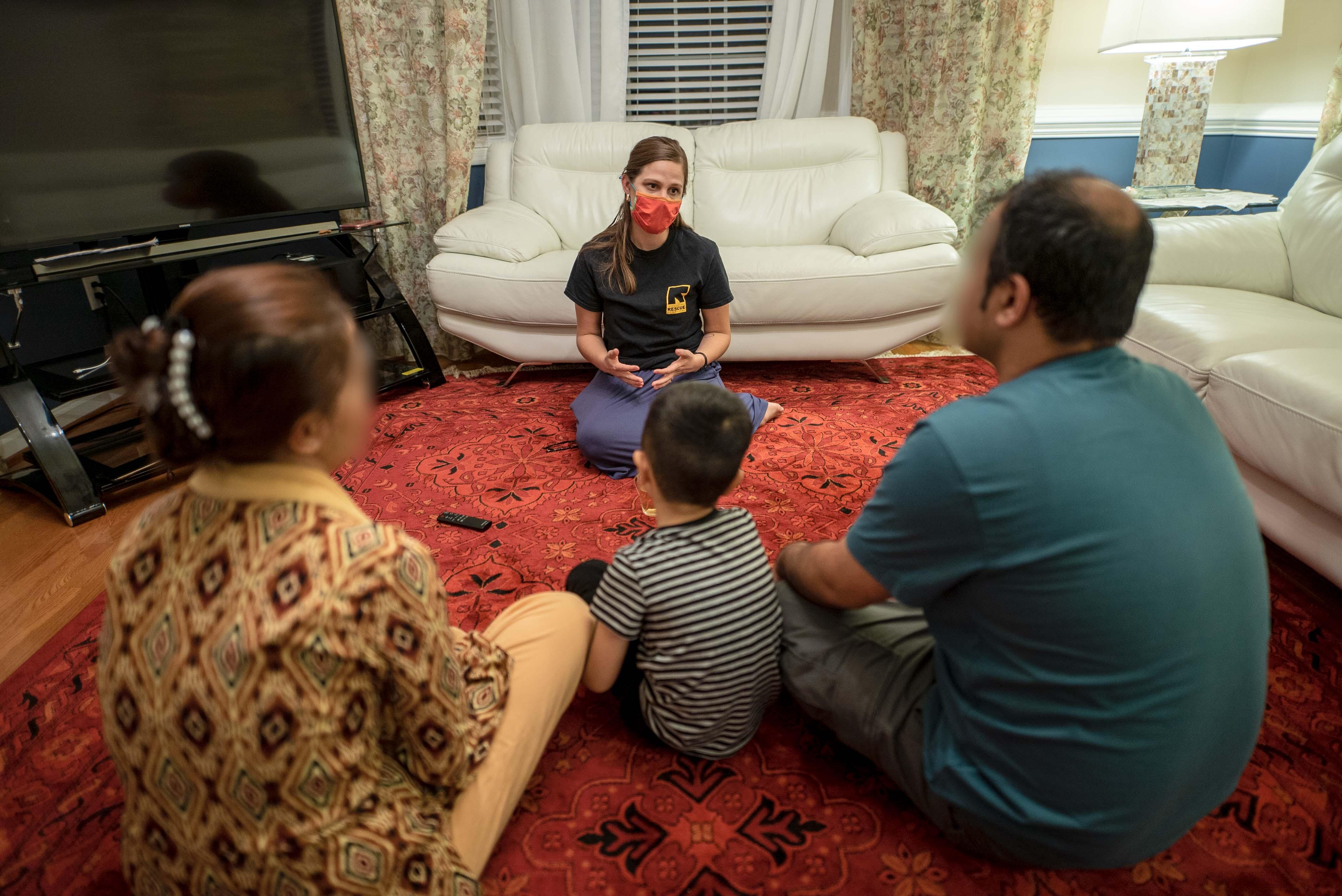 An IRC staff member sits and speaks with an Afghan man, woman, and child.