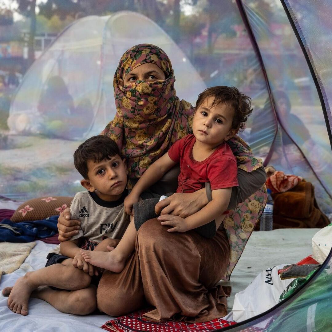 A recently widowed Afghan woman, 28, sits on the floor of a net tent holding holding her two children in a makeshift camp for displaced families in Afghanistan.