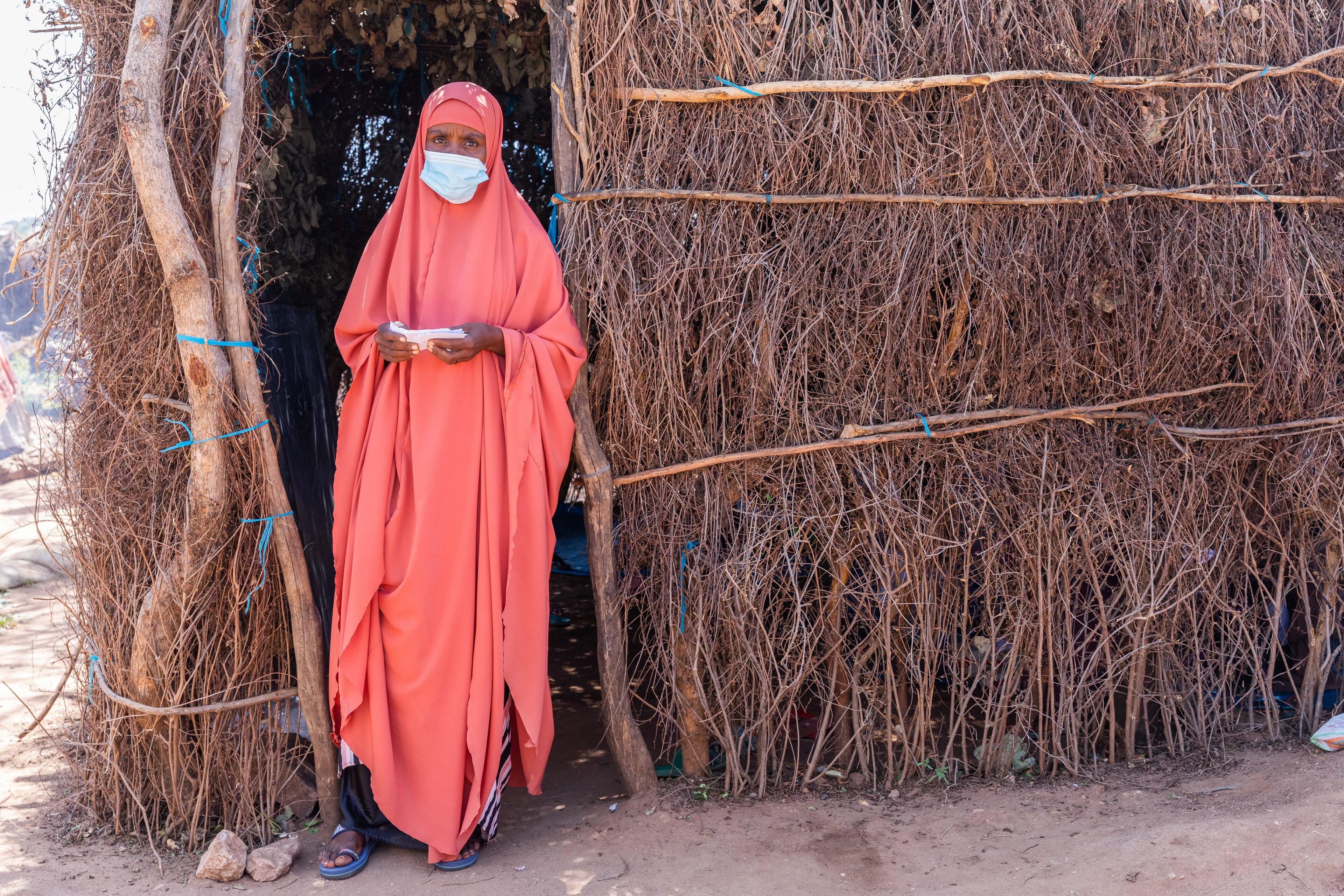 A teacher wearing a mask to protect against the spread of COVID-19 stands outside her makeshift classroom fashioned from branches in a displacmeent camp in Ethiopia.