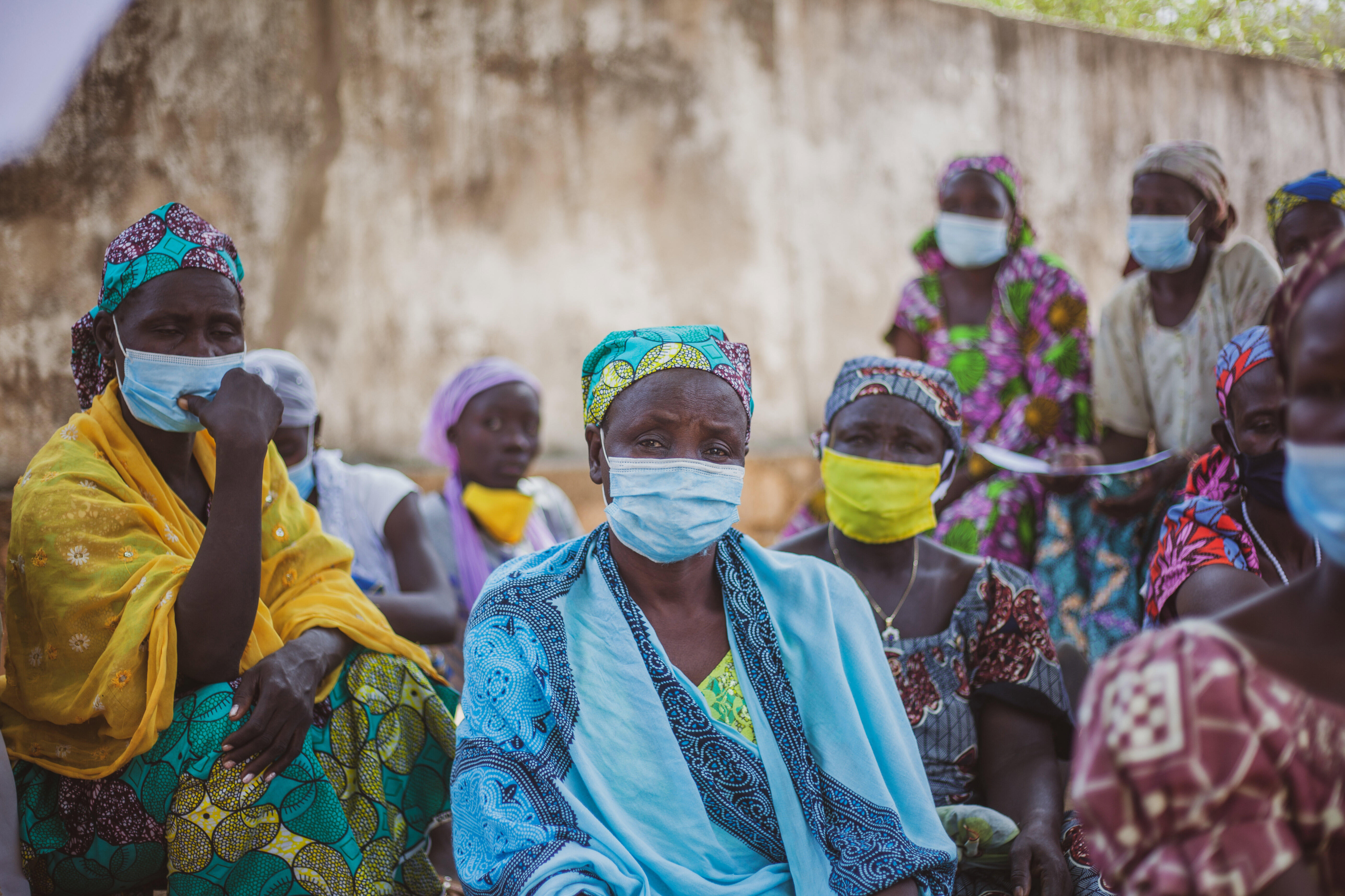 Zara, a 54-year-old woman, sits in the forefront surrounded by other women, all wearing masks. 