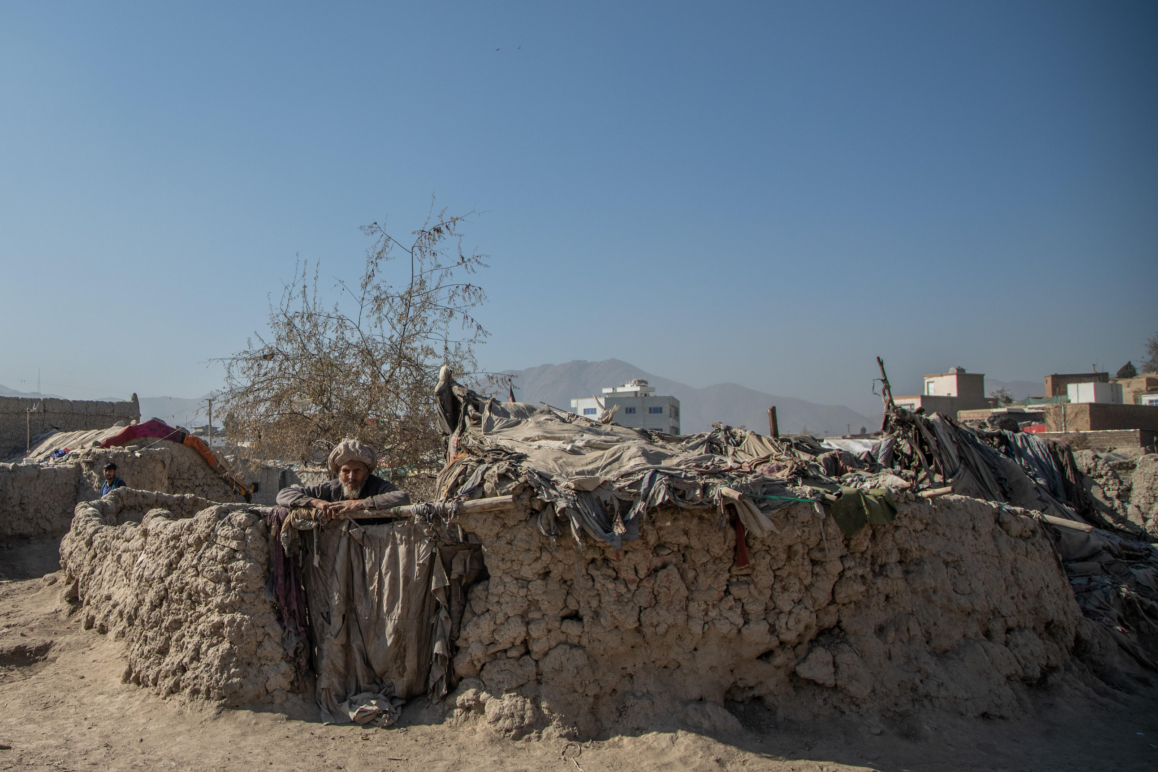 An elderly Afghan man leans on a low wall outside his makeshift home in a camp near Kabul where the IRC is providing emegency cash to displaced families.