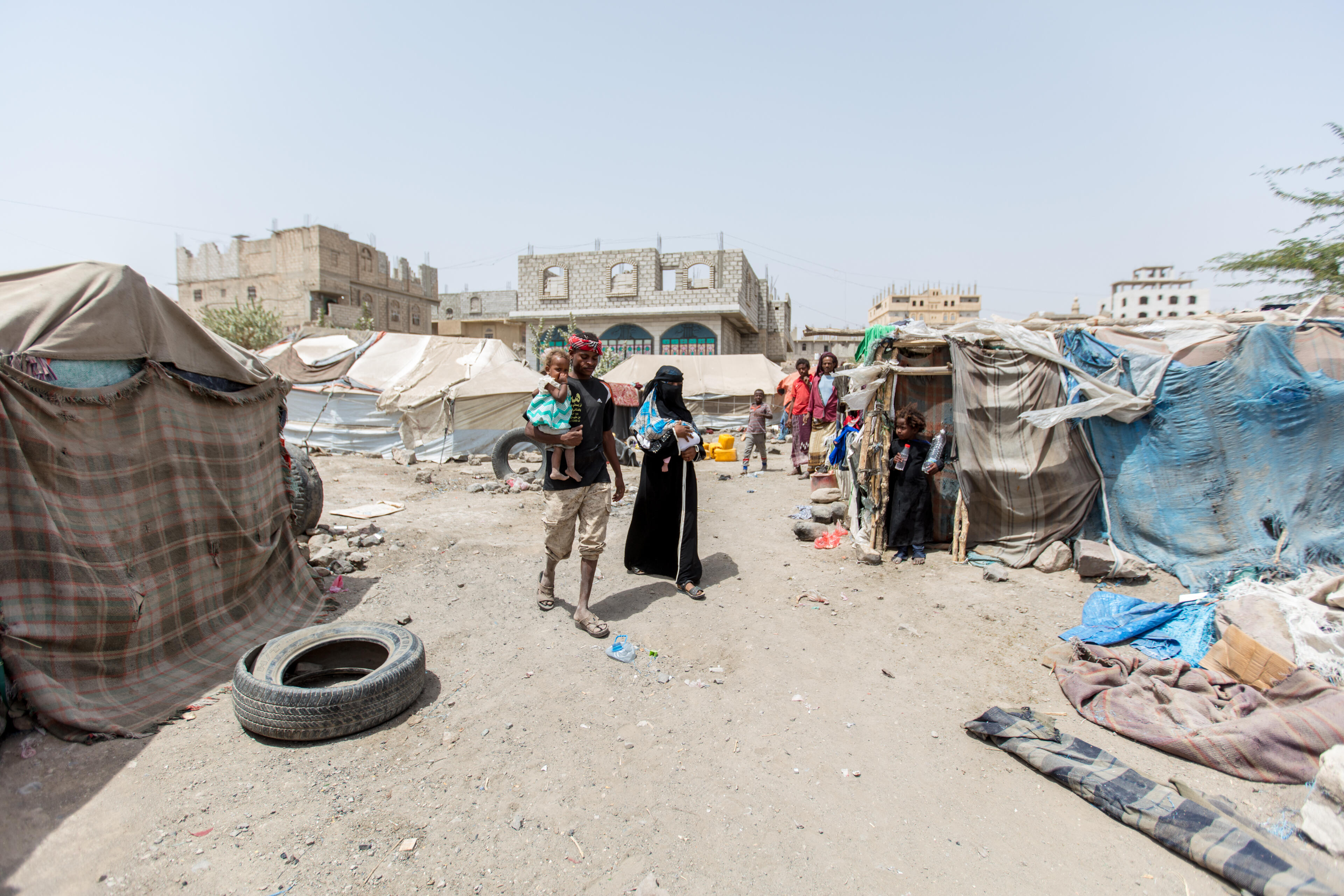 Bodor, carrying her infant daughter walks with her husband and toddler through the camp where they live in a tent alongside other families displaced by the war in Yemen.