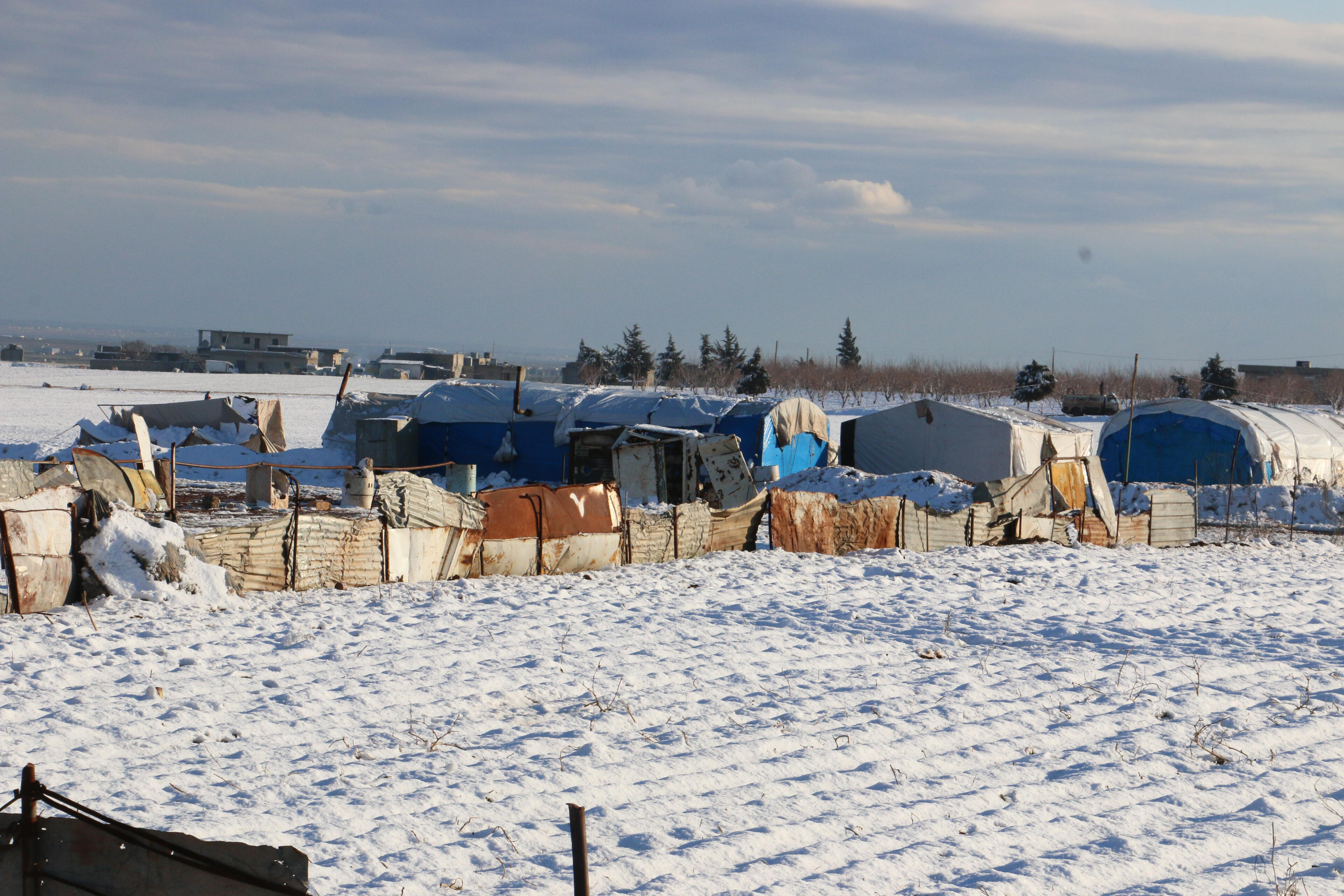 Makeshift shelters housing displaced Syrian families are huddled together in a snow-covered field.