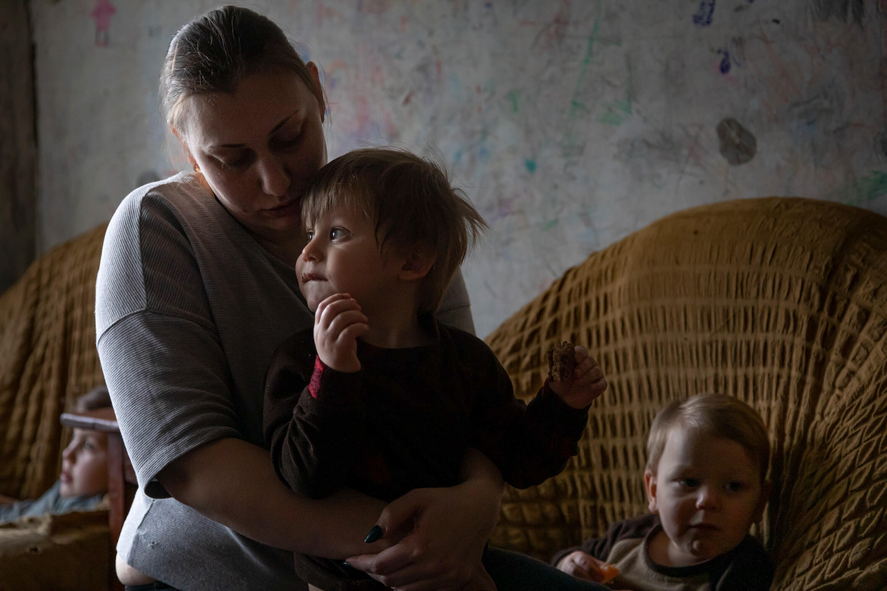 A mother sits holding one of her sons on her lap. Two other children sit in chairs behind them. 