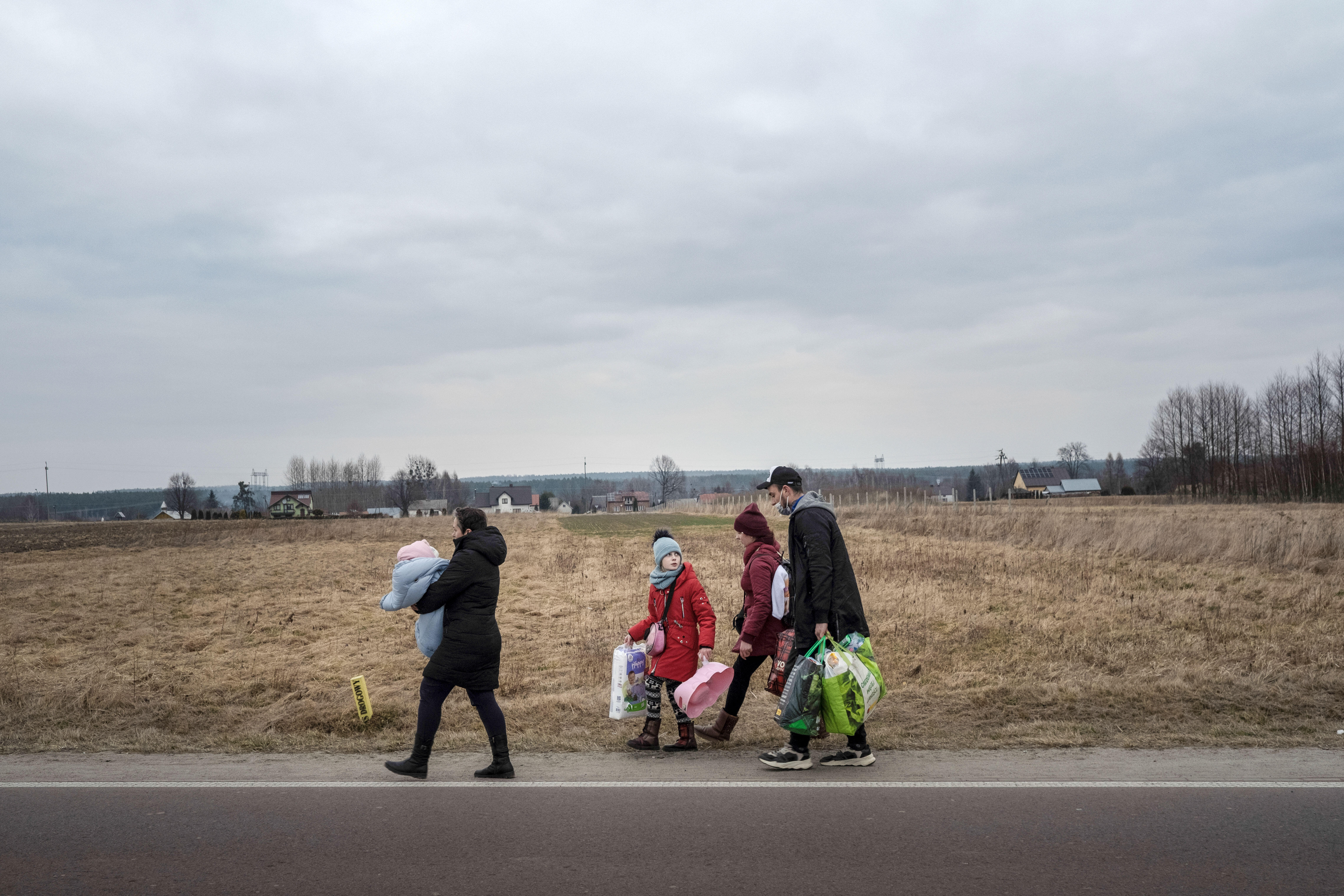Landscape shot of a family walking down a road carrying bags. There are two adults and two children. 