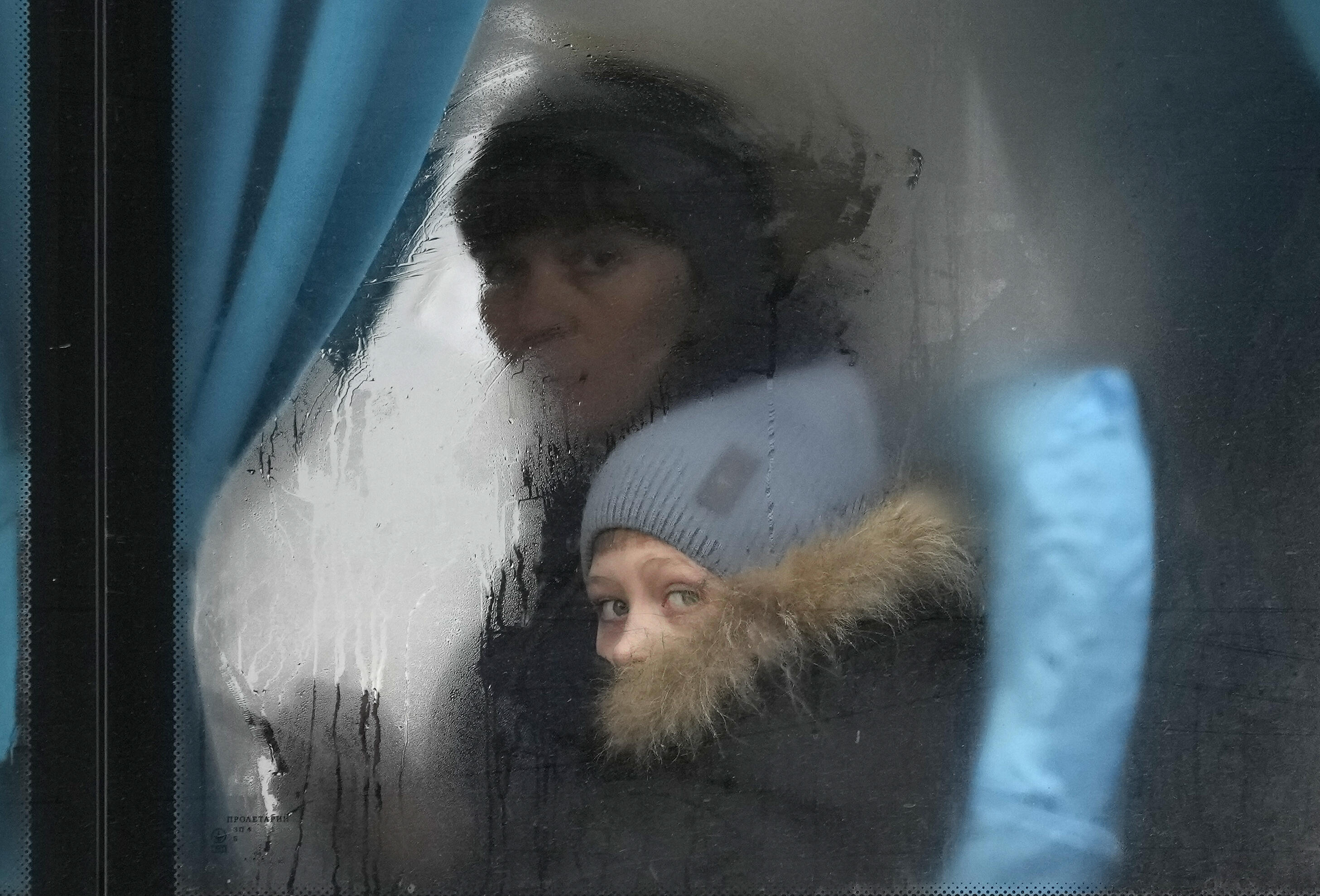 The smudged window of a bus with a woman and child peering out of it. They are wearing winter hats and coats. 