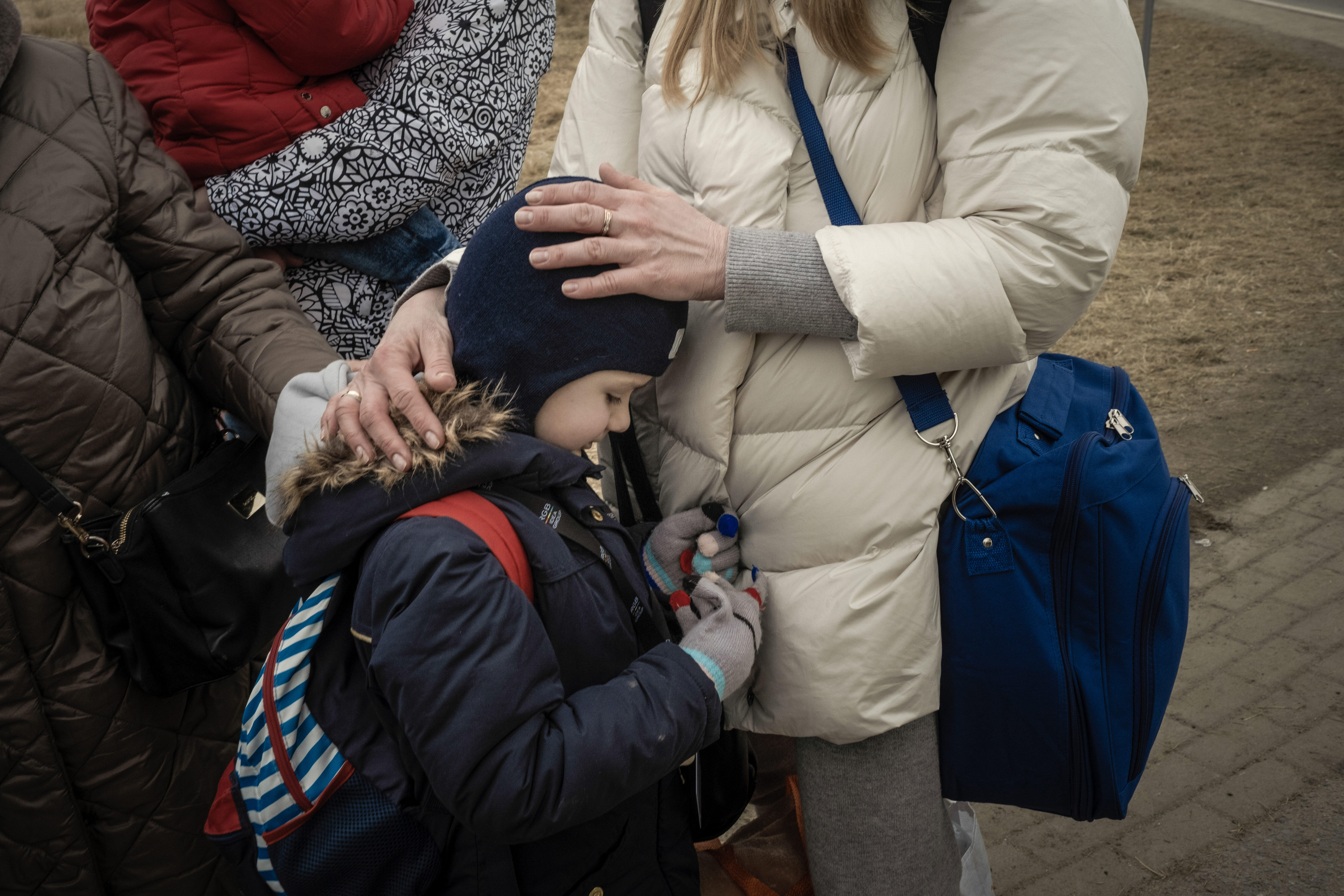 A close up of a child leaning on their mom while she rests her hands on their head.