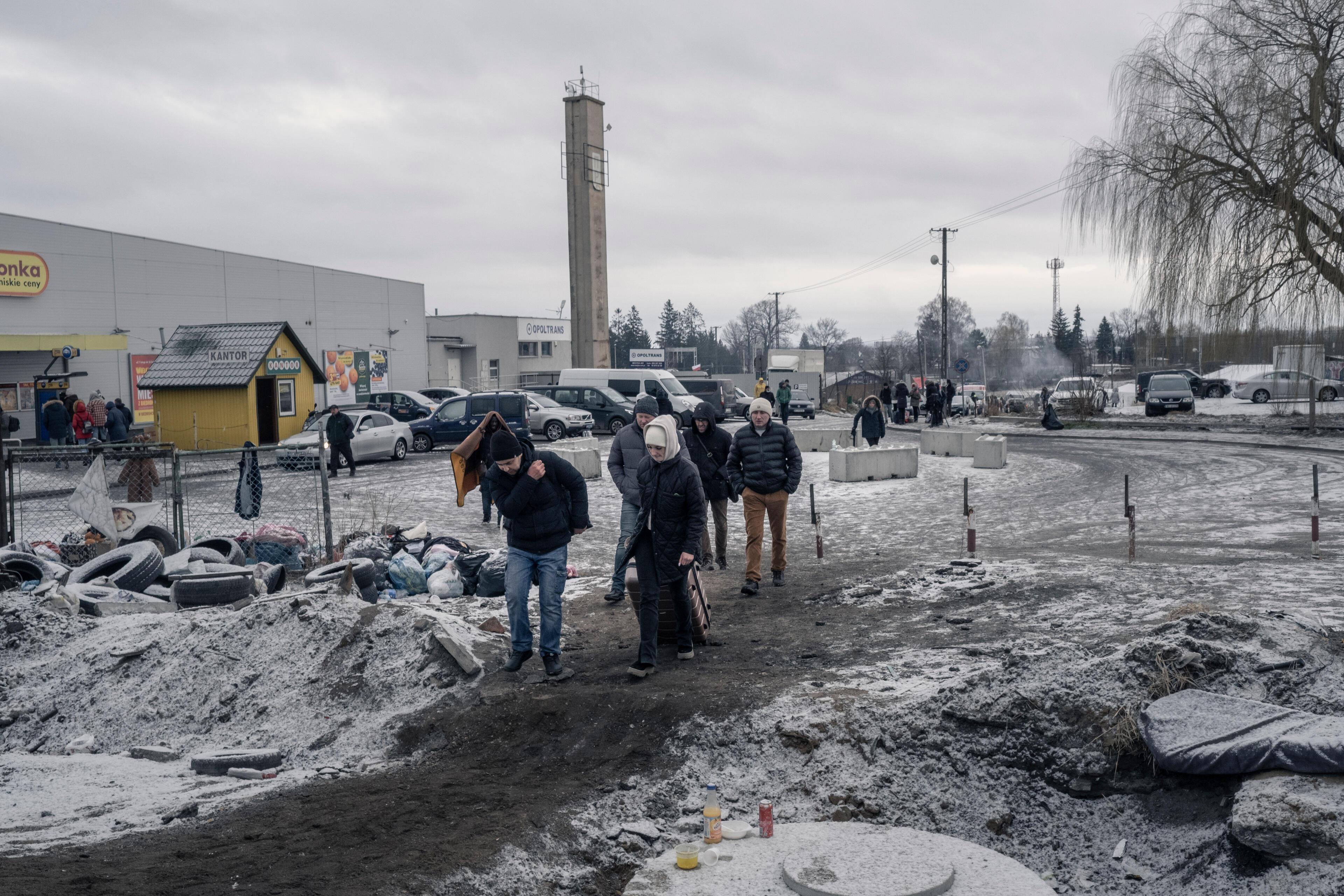 A small group of people who fled Ukraine carry small items of luggage as they walk through an industrial area after crossing the border into Poland.