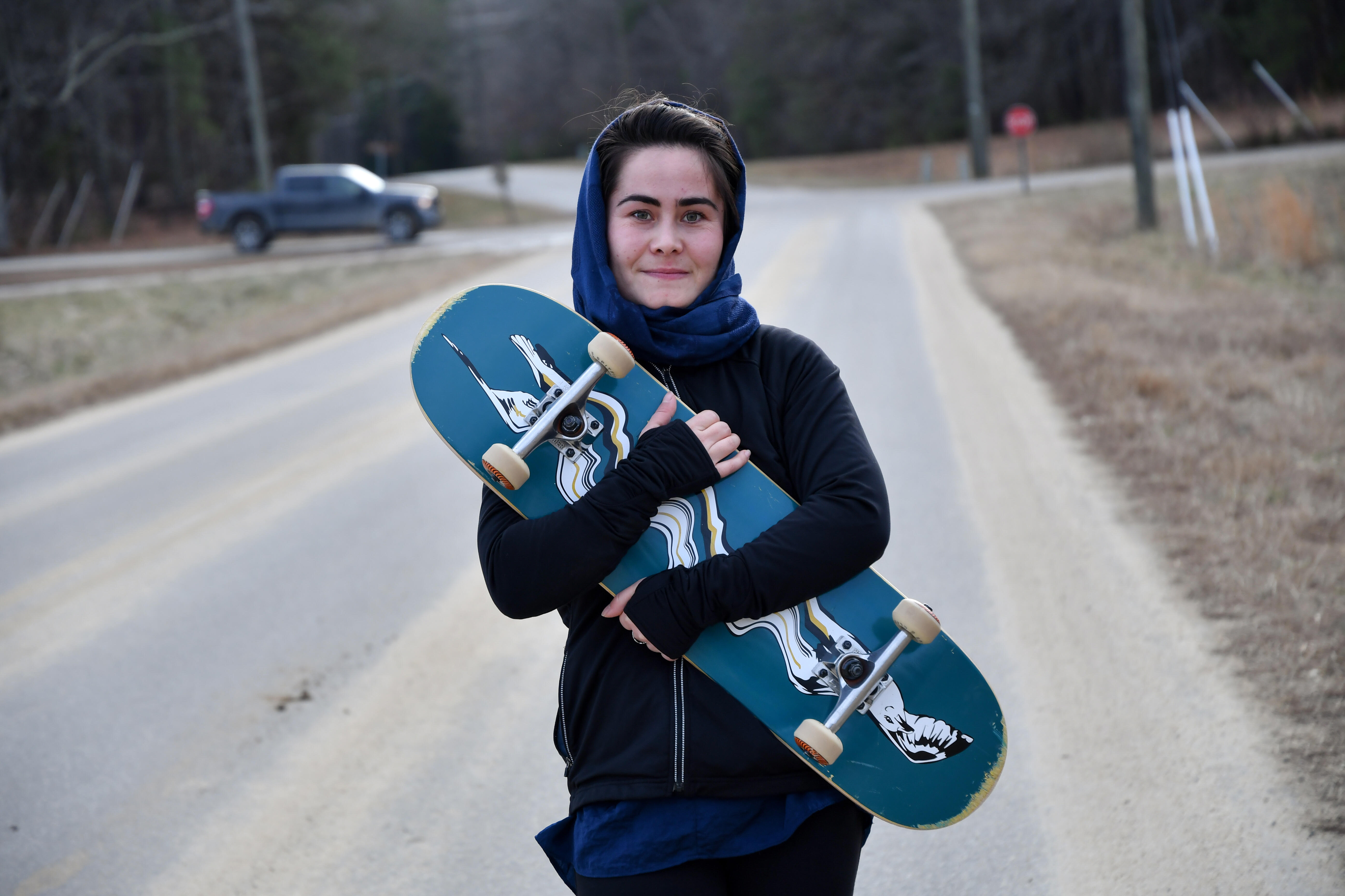 Belqisa holds her skateboard to her chest and smiles 