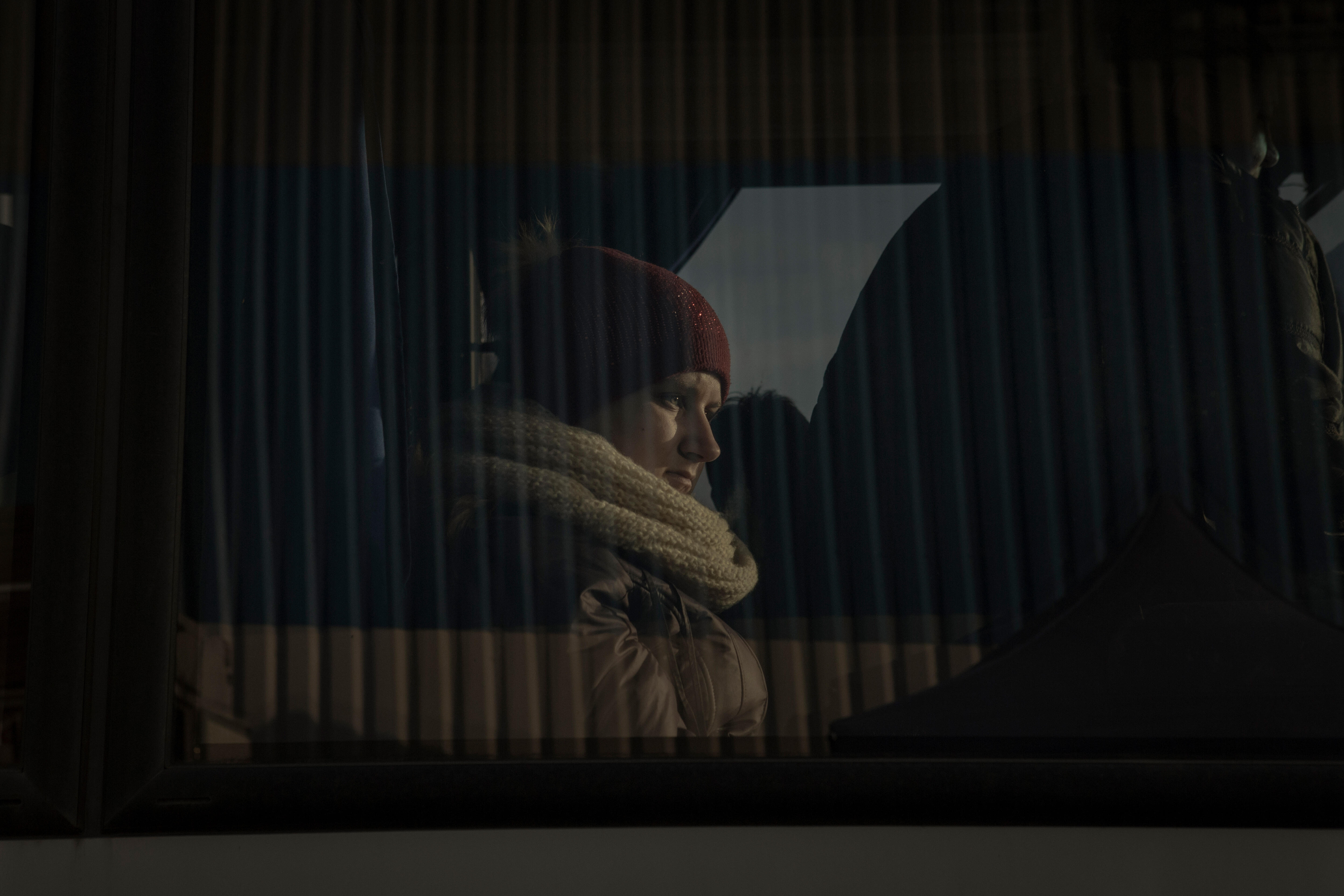 A woman sits in a bus wearing winter clothes and looks out the window. 