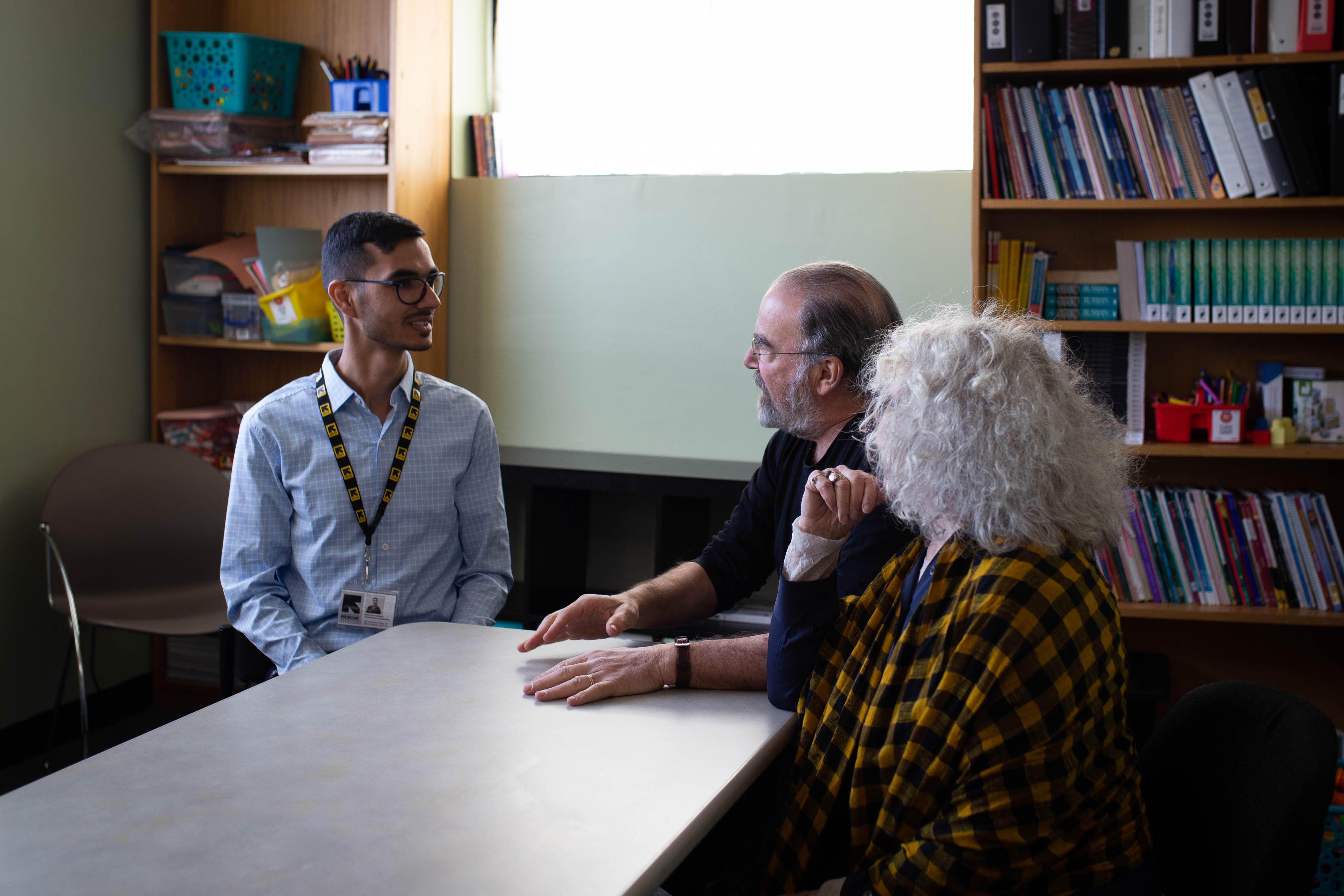 Mandy Patinkin and Kathryn Grody talk with Shir Zad Sarbaz while sitting at a table in the IRC New Jersey office