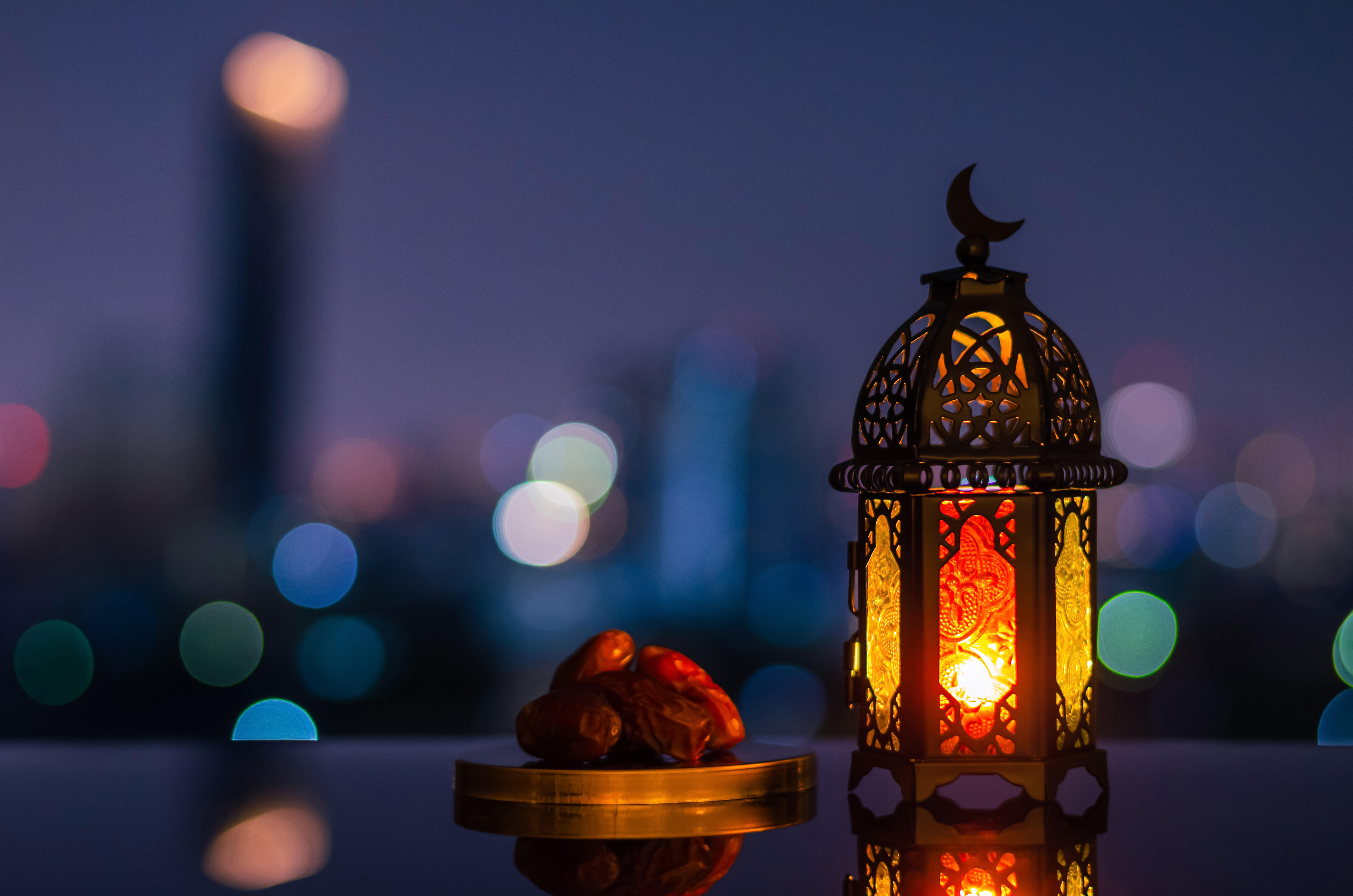 A lantern that has moon symbol on top and small plate of dates fruit with night sky and city bokeh light background for the Muslim feast of the holy month of Ramadan.