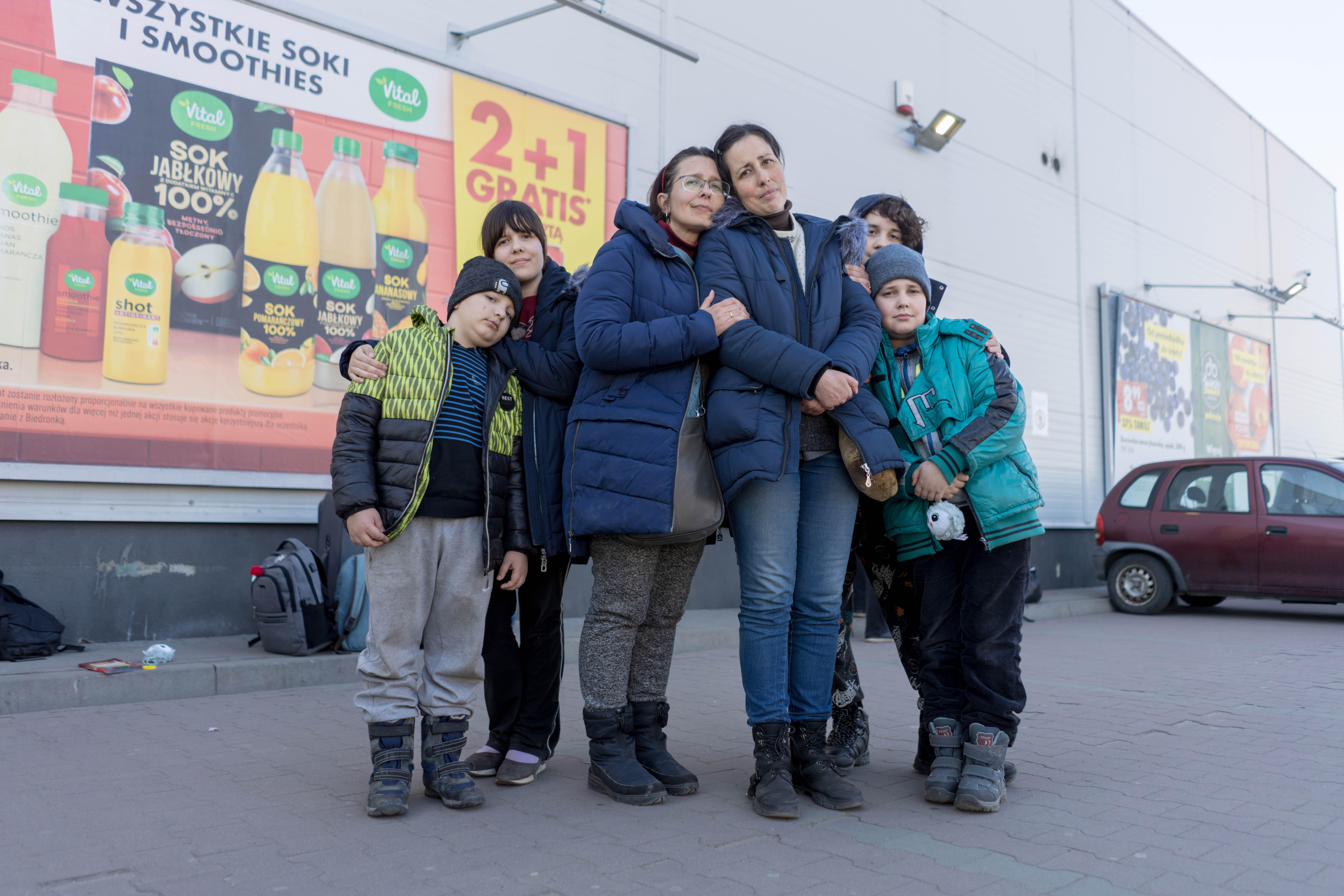 Two women surrounded by their children, all are wearing winter clothes and looking at the camera. 