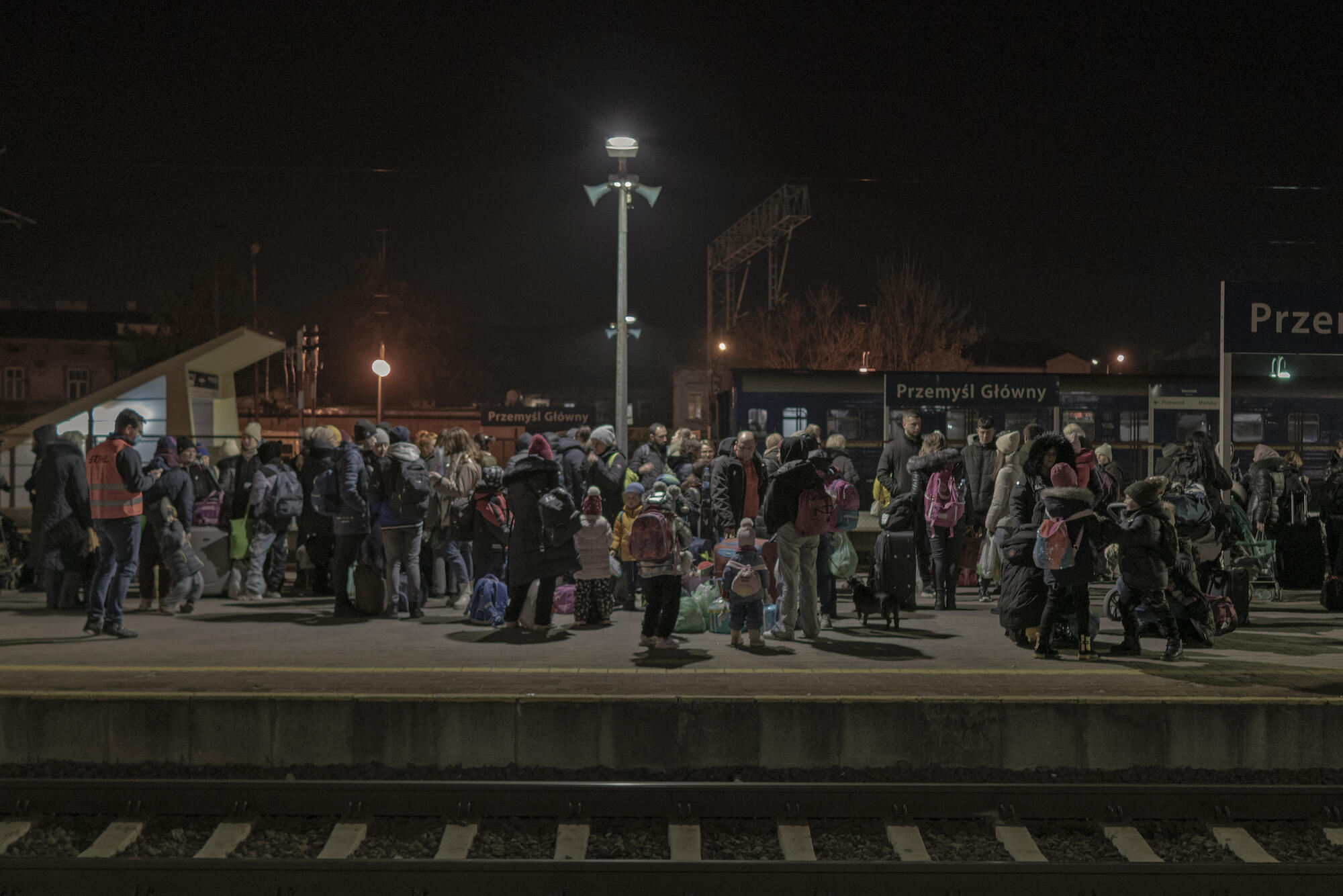 A group of many people stand outside on a train station platform.
