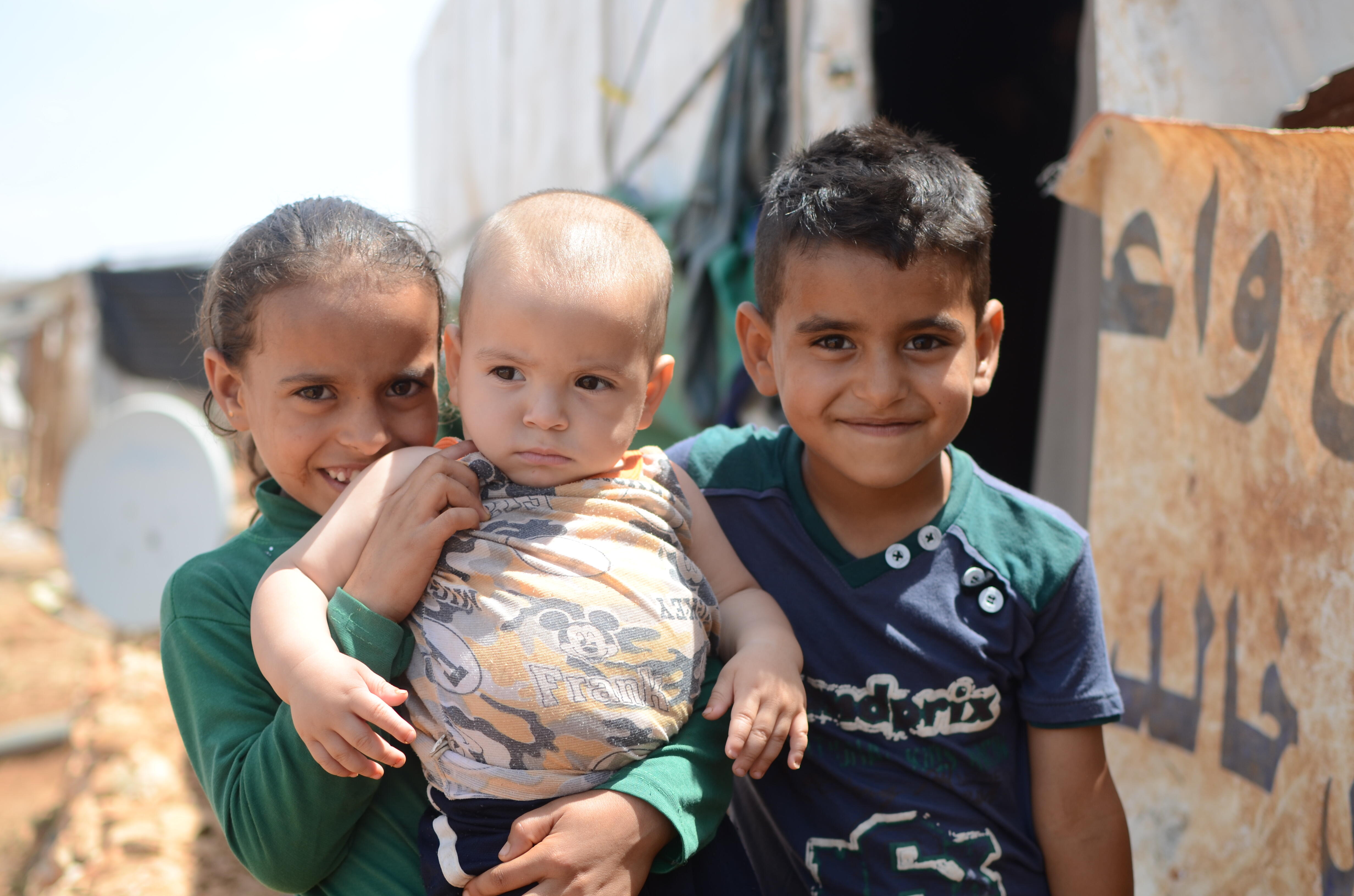 Two Syrian children hold a baby outside a tent in a refugee settlement in Lebanon