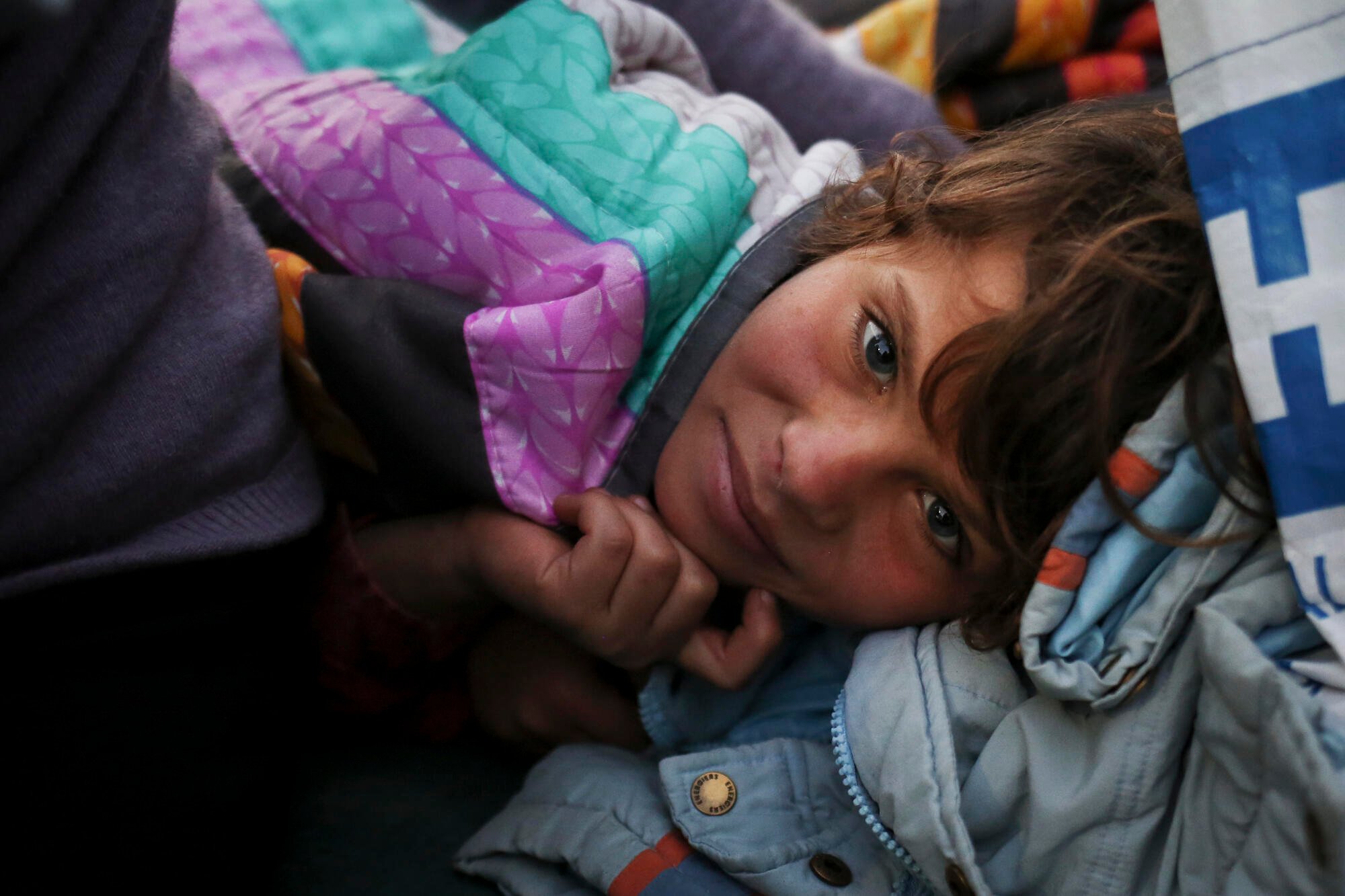 A Syrian refugee girl stays warm in blankets inside a tent in Greece