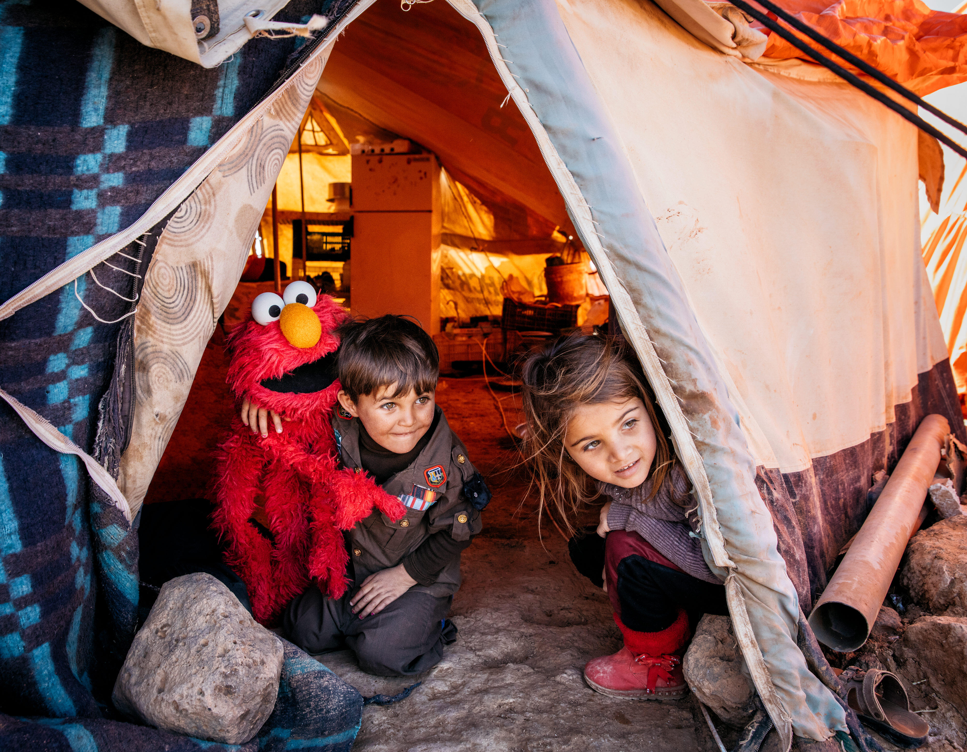 A young Syrian boy and girl  with a Sesame Street Elmo puppet in their tent in a refugee camp in Jordan