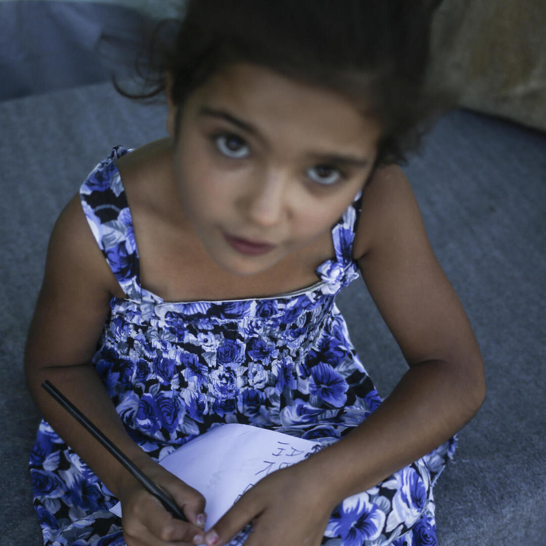 A young Syrian refugee girl writes in a notebook.