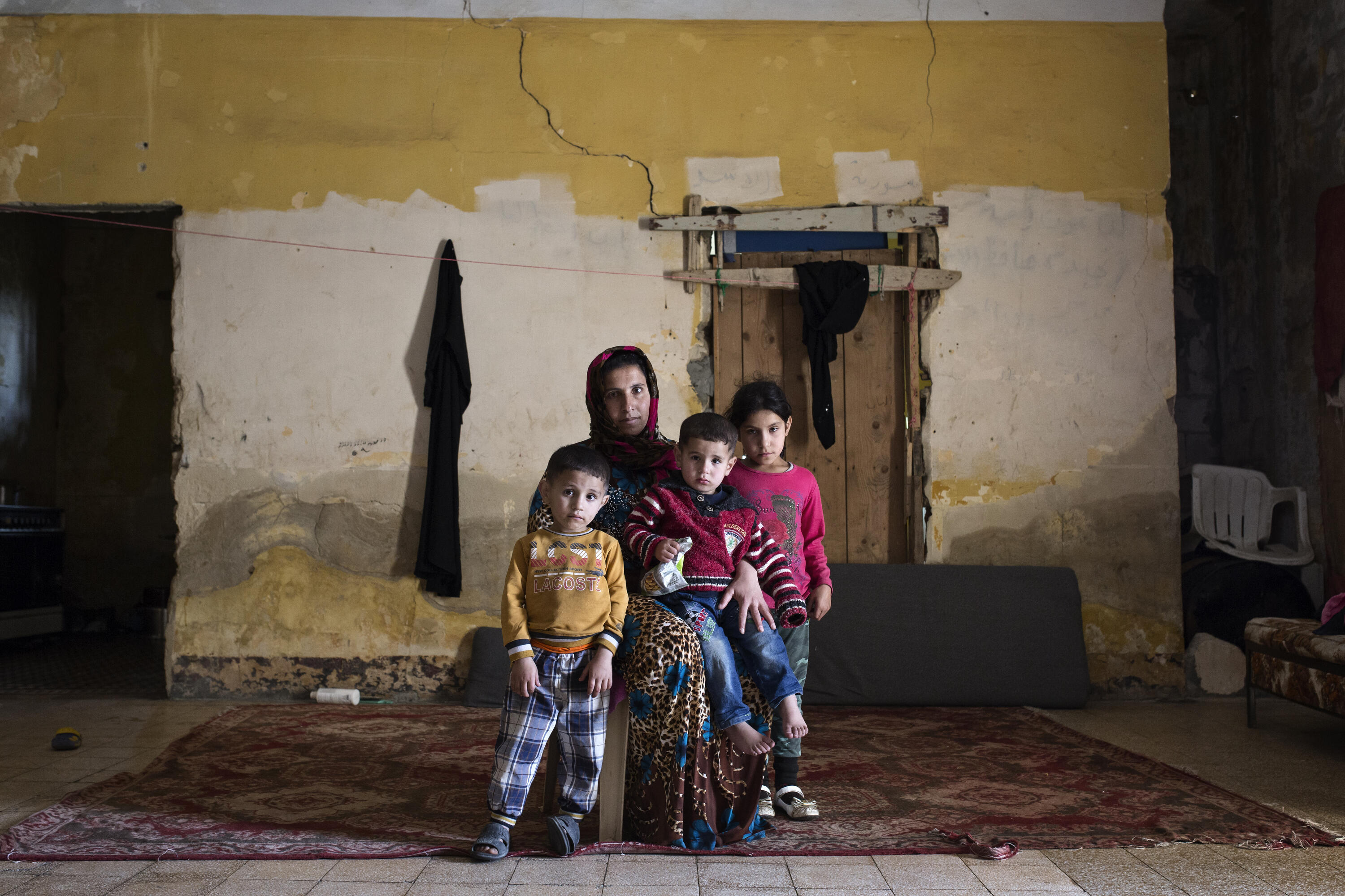 A Syrian mother and three children sit amid rubble in an abandoned building where they live as refugees in Lebanon. 