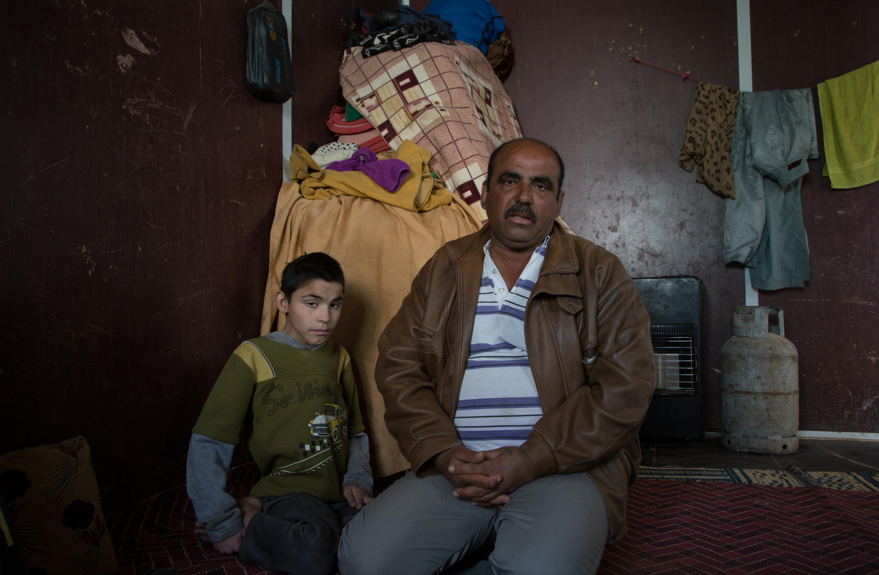 Abu Raed sits with his son Bashar, who is paralyzed, in their family's caravan at the Zaatari refugee camp in Jordan.