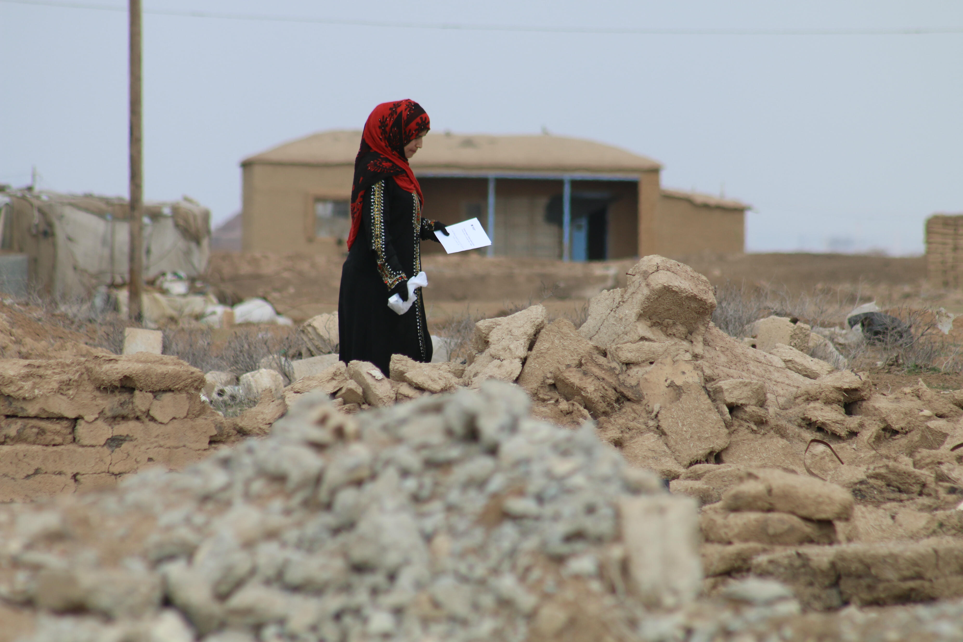 A woman picks her way through the rubble of her village in Northeast Syria, carrying a bag of prescription medicine that she received from an IRC mobile clinic.