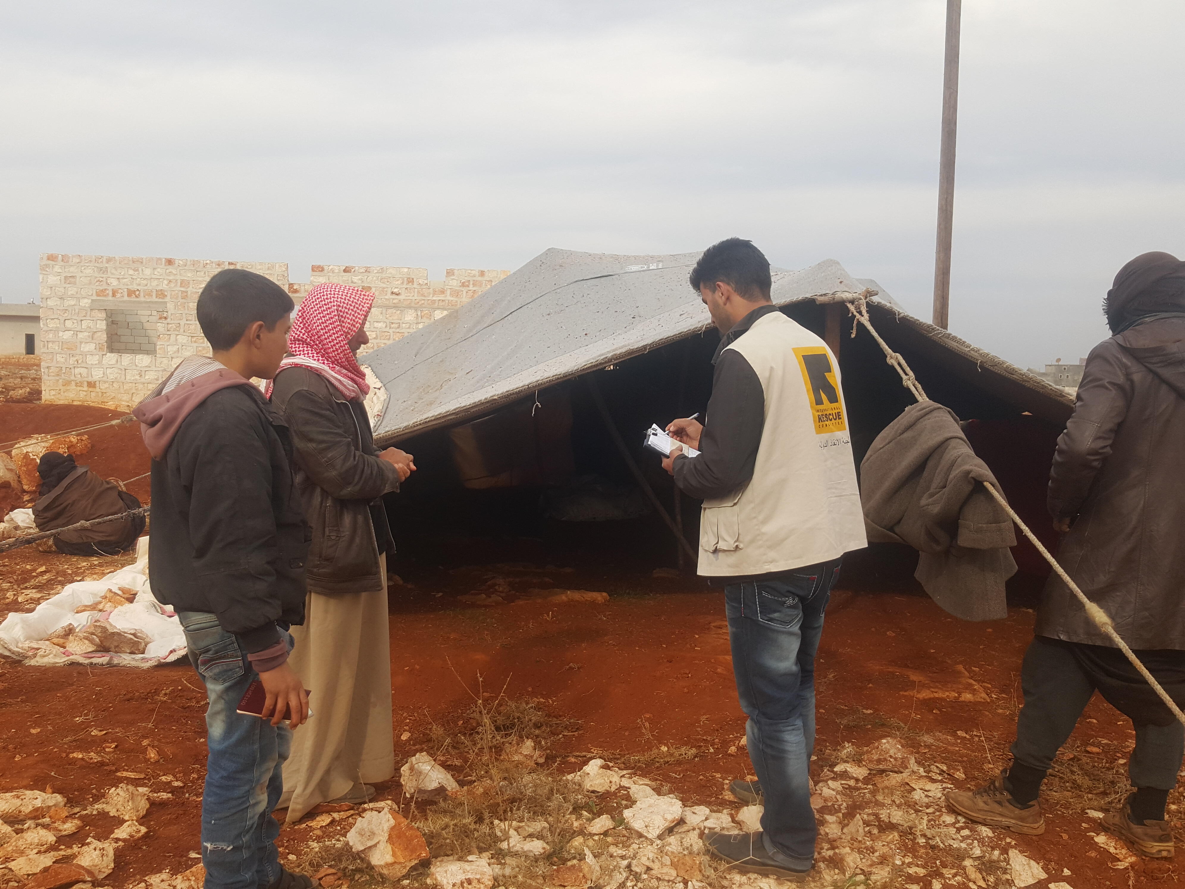 An IRC aid worker speaks with a man whose family was displaced in Syrias Idlib province and living in a tent